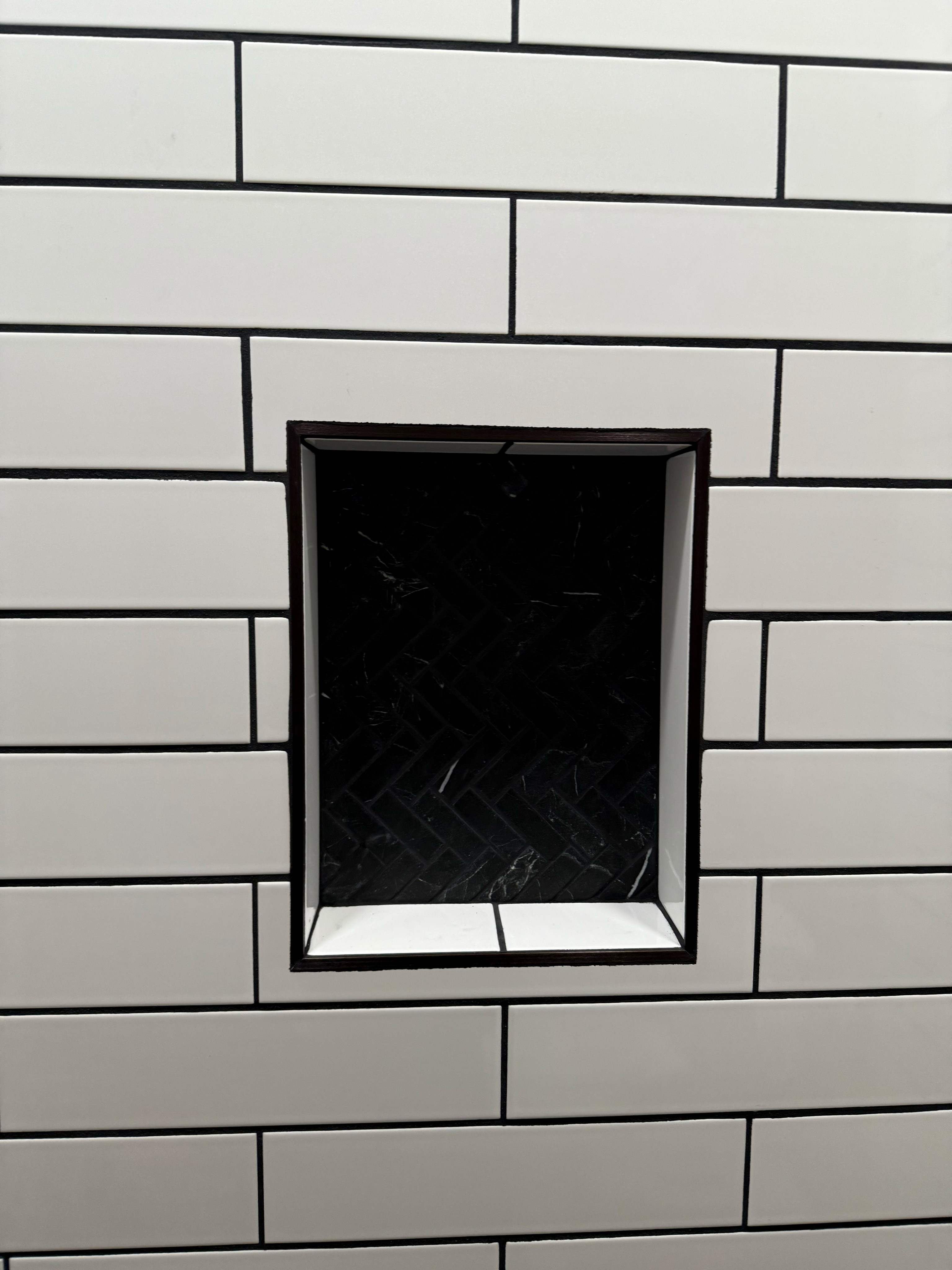 Detailed view of a custom shower niche with white subway tiles and black grout, showcasing a sophisticated black herringbone mosaic tile interior.