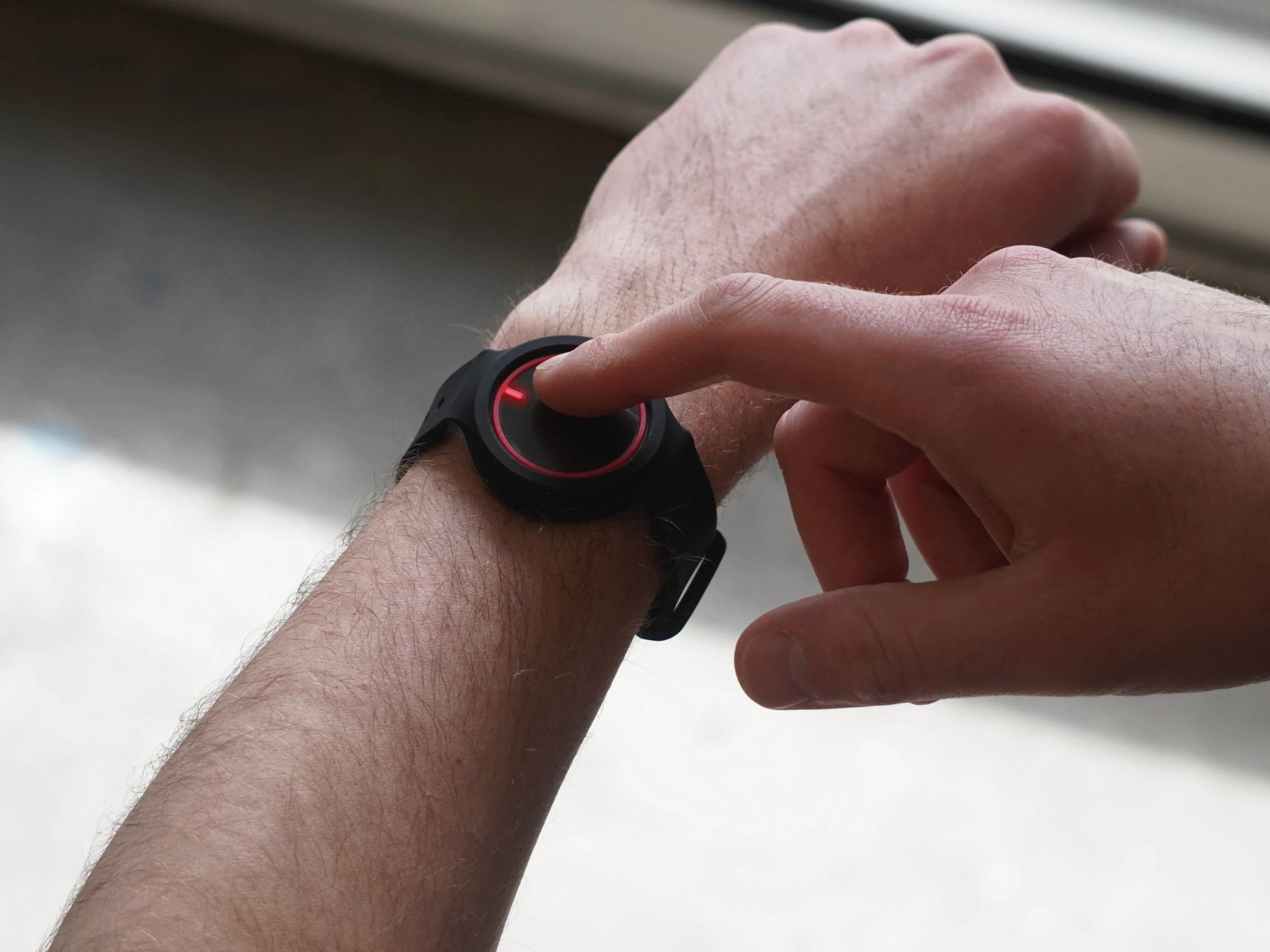 B10 wearable device worn on a wrist with the user pressing the button to indicate an emergency