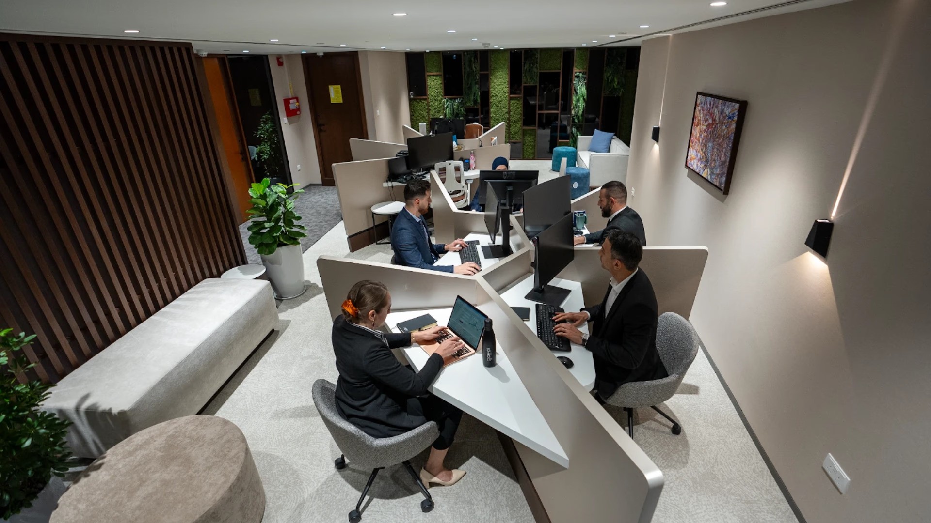   بيئة عمل عصرية ومضاءة جيدا لموظفين يعملون على مكاتب حديثة ومنظمة، توضح الأجواء المهنية المناسبة لعمل الشركات الاجنبية في السعودية والشرق الأوسط مع لمسات ديكور نباتية.