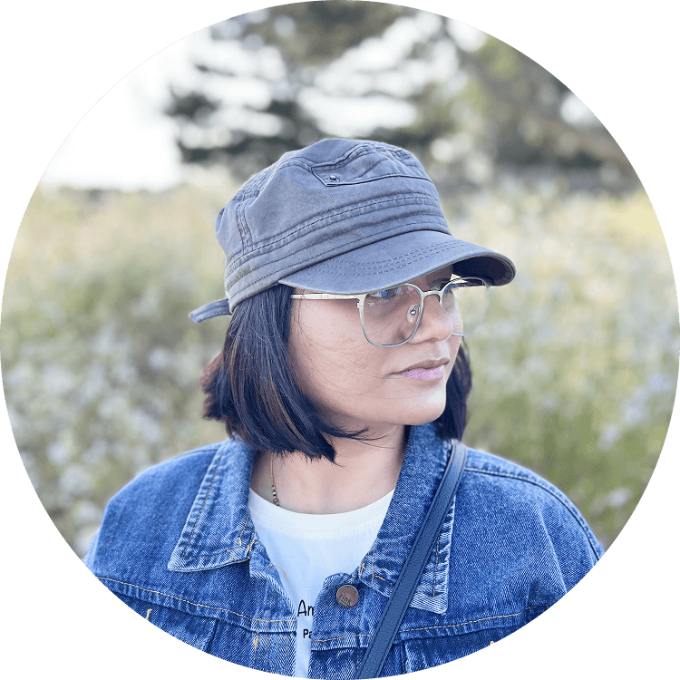 Person wearing a blue puffer jacket and red backpack standing in front of a light blue building on a city street.