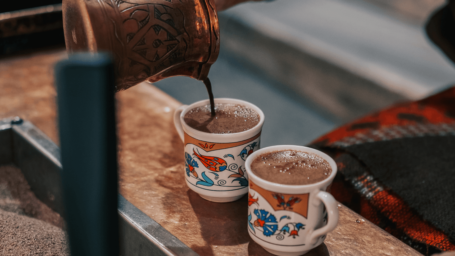 Traditional Turkish coffee being poured from a copper cezve into ornate ceramic cups, brewed in hot sand for a rich and authentic flavor.