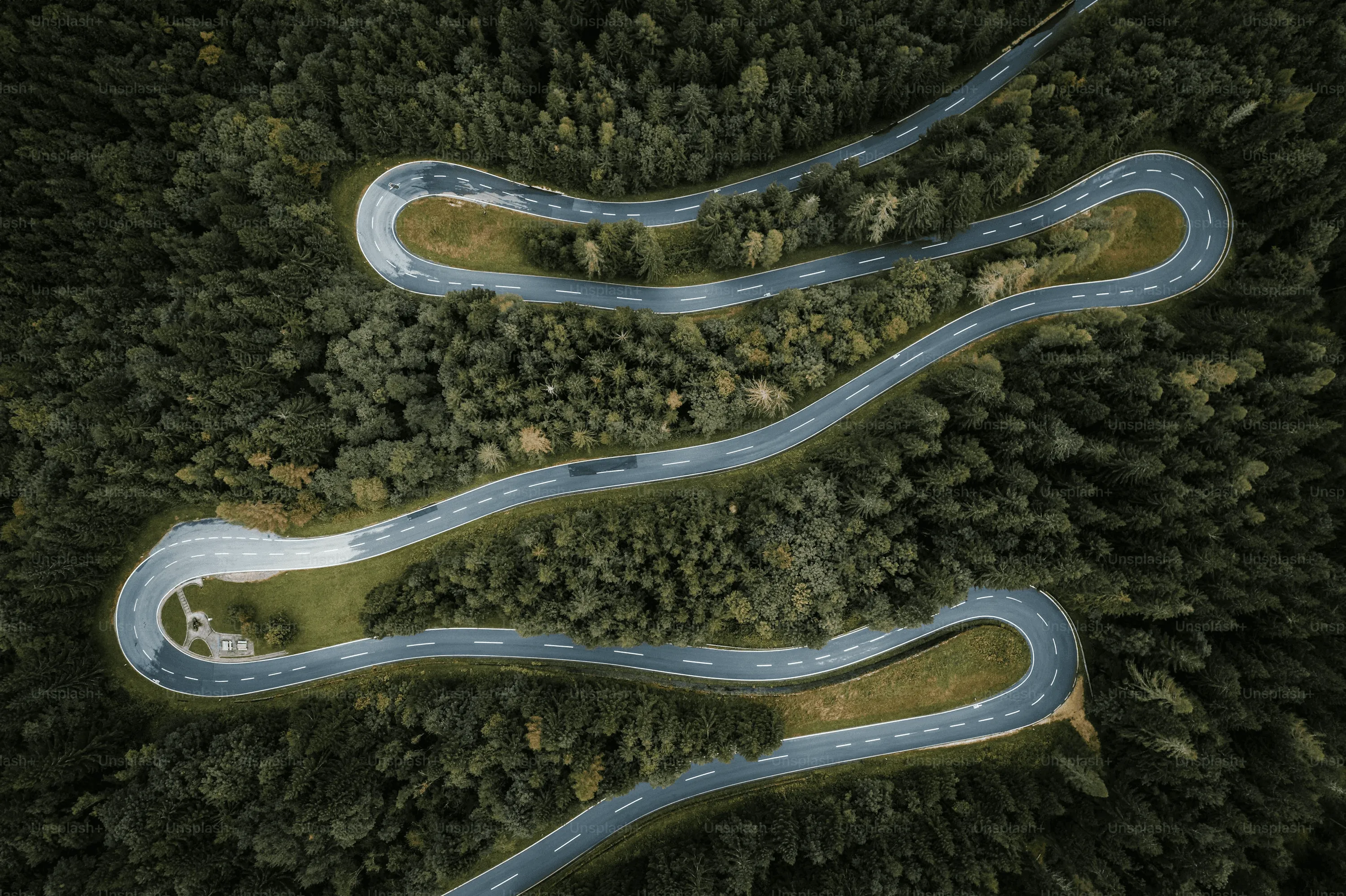 A winding road cuts through rocky terrain, surrounded by patches of green grass and illuminated by sunlight.