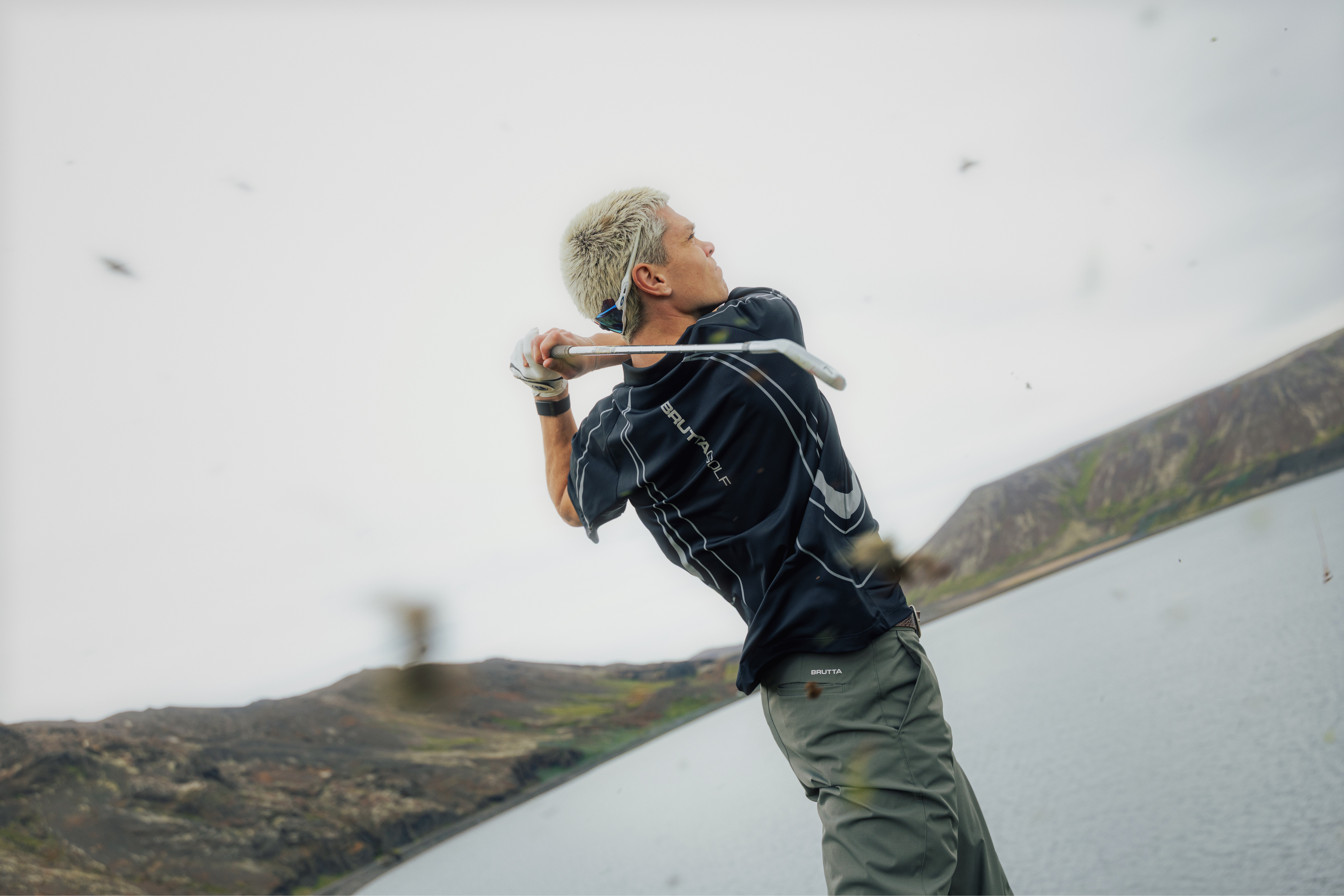 Low-angle view of a golfer's follow-through against an overcast Icelandic sky