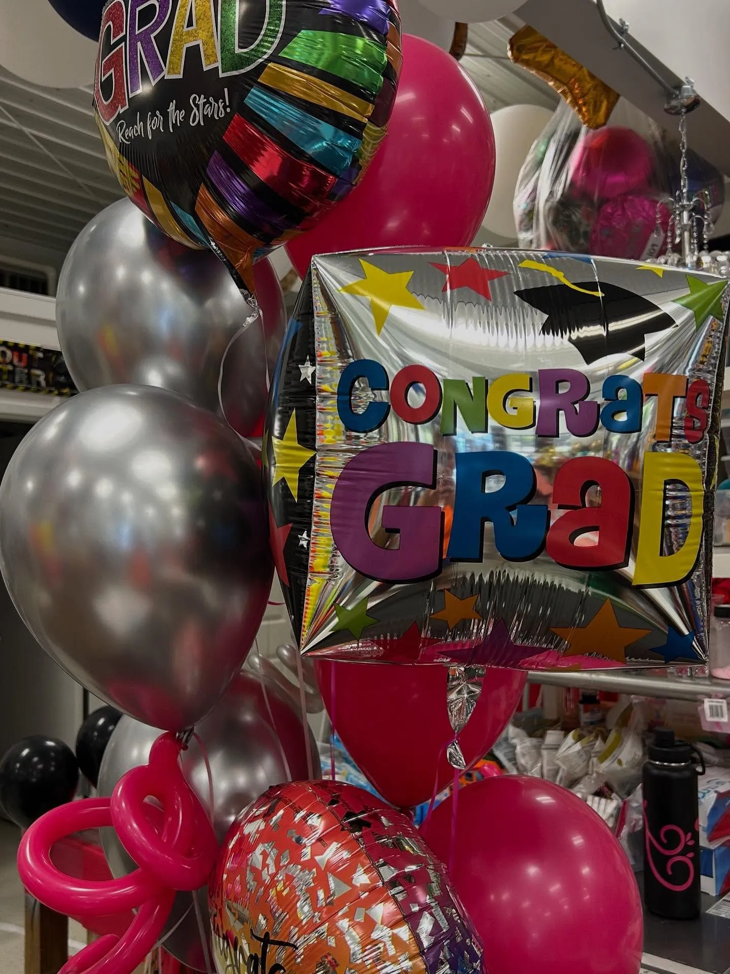 A colorful display of congratulatory graduation balloons, featuring vibrant designs with phrases like "Congrats Grad," amid a variety of metallic and pink helium balloons, enhances the celebratory atmosphere in a festive setting.