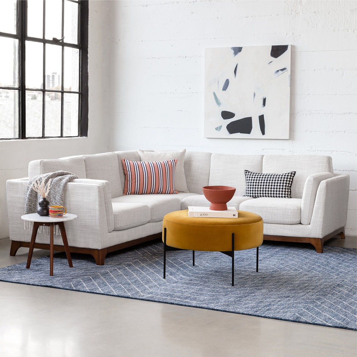 Ceni sectional sofa with contrasting pillows, paired with a round yellow ottoman and modern art