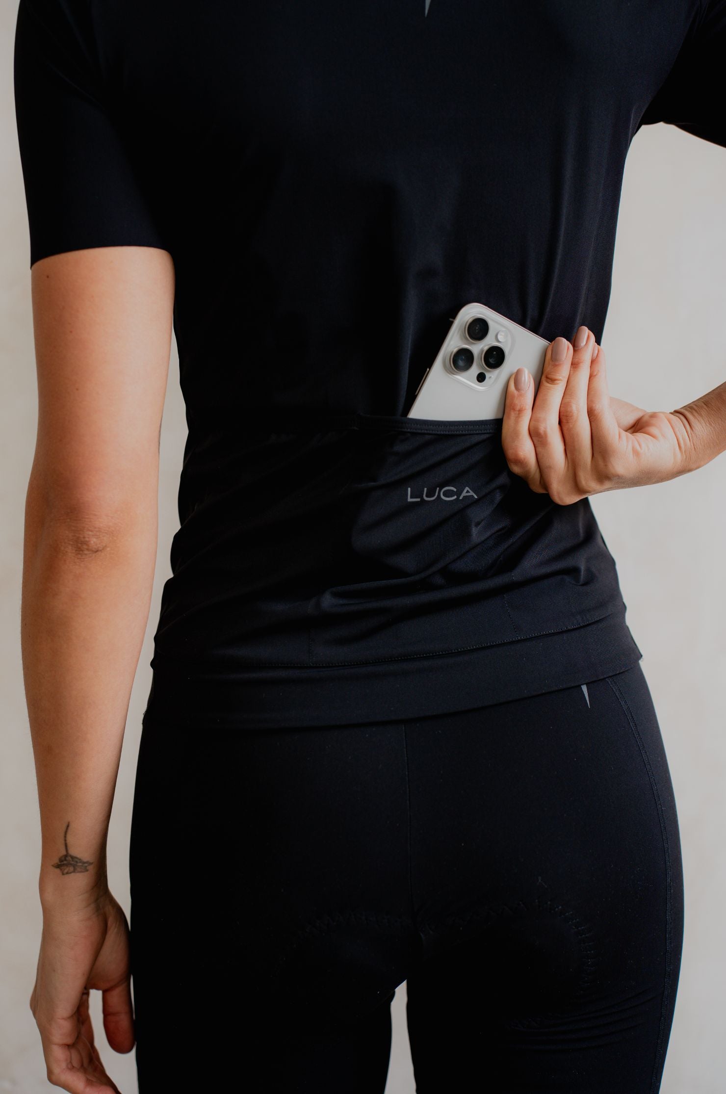 Person-wearing-a-LUCA-Solstice Jersey- Black-and-black-pants-holding-a-white-phone-with-three-camera-lenses-against-their-torso
