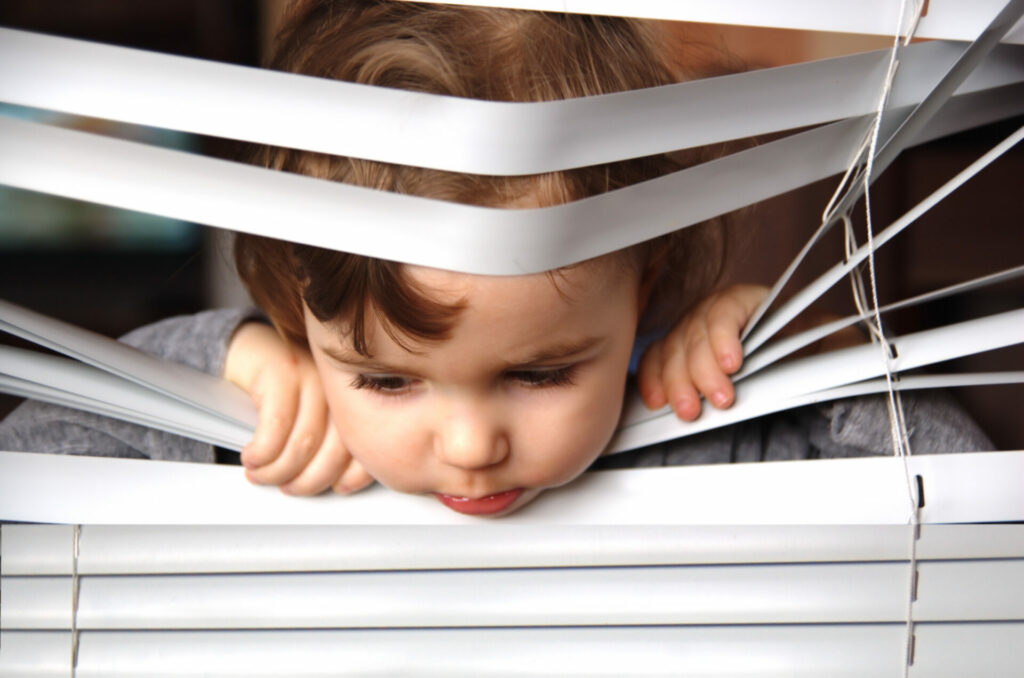 Child sticking their head through window blinds 