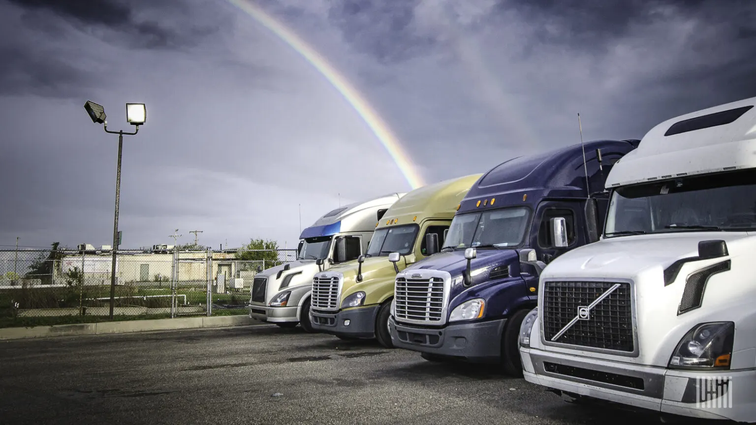Row of parked semi-trucks under a rainbow after rain