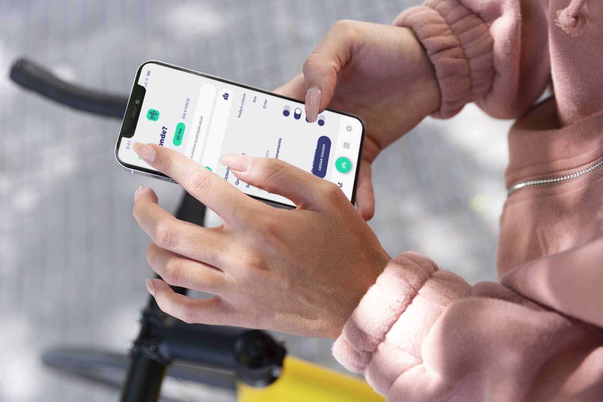 A person holds a smartphone displaying a map or app, with a bike in view.