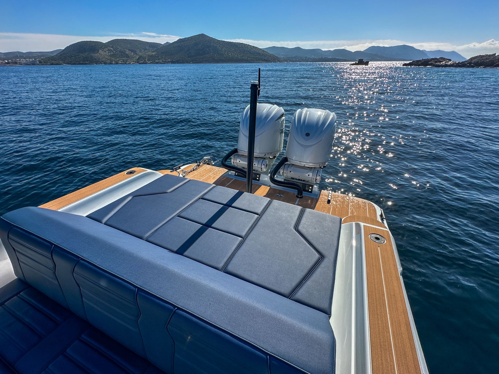 White Rock 36 speedboat with captain at helm cruising calm blue waters near Paros coastline with hills in background.