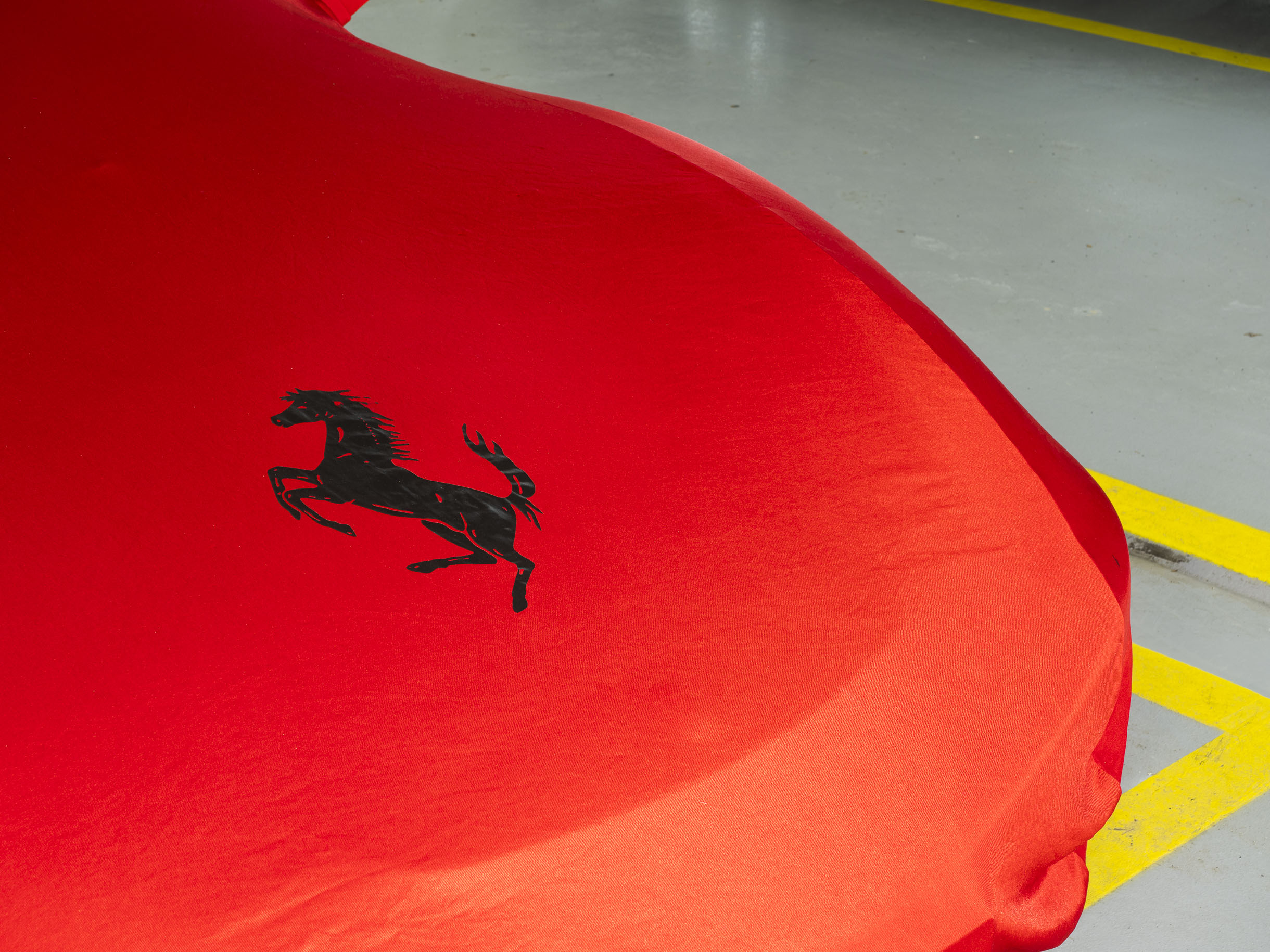 Gros plan sur le capot d'une Ferrari recouvert par une couverture rouge de la marque et d'un gros logo Ferrari