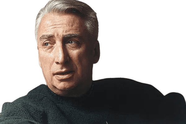 A color portrait of a middle-aged man with neatly combed silver hair, wearing a dark sweater and looking to his left with a thoughtful expression. The image captures a contemplative mood, with soft, natural lighting highlighting his face against a neutral background, emphasizing his intellectual presence.