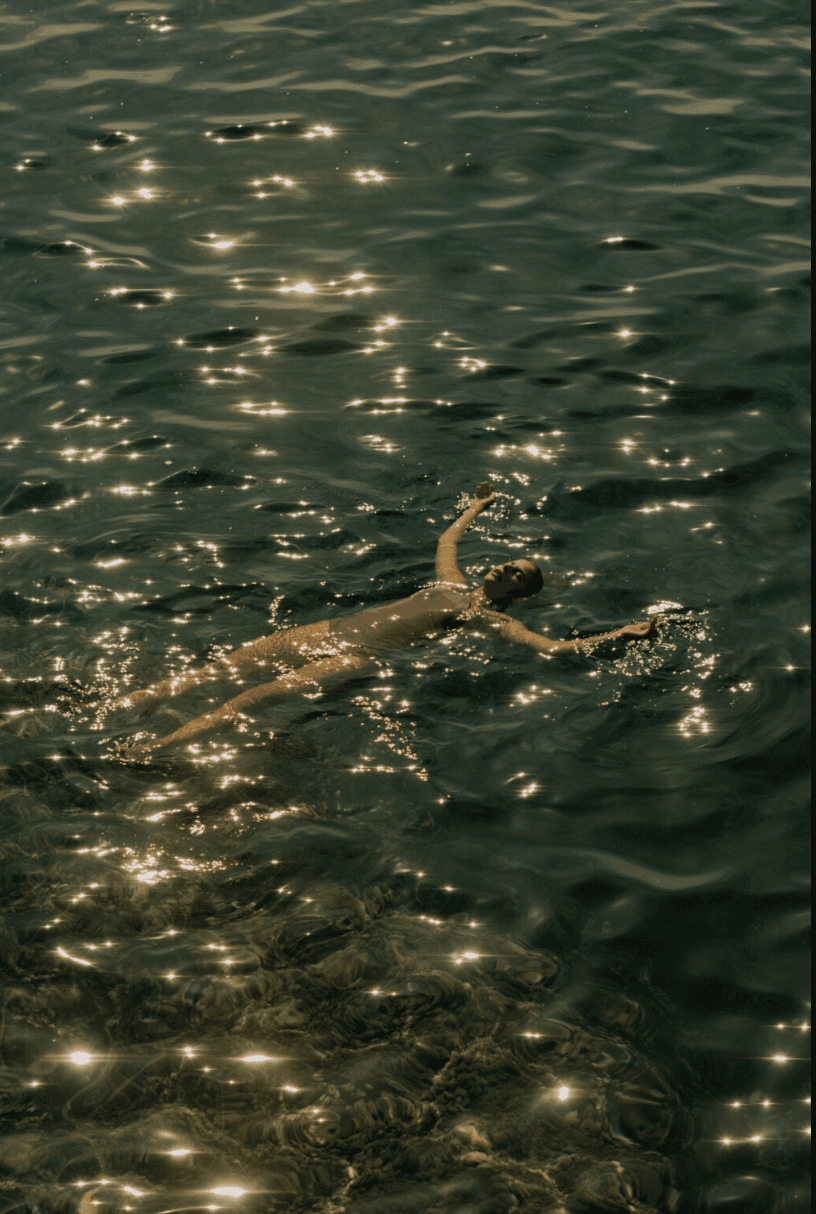 a woman relaxing by levitating in the sparkling sea at golden hour