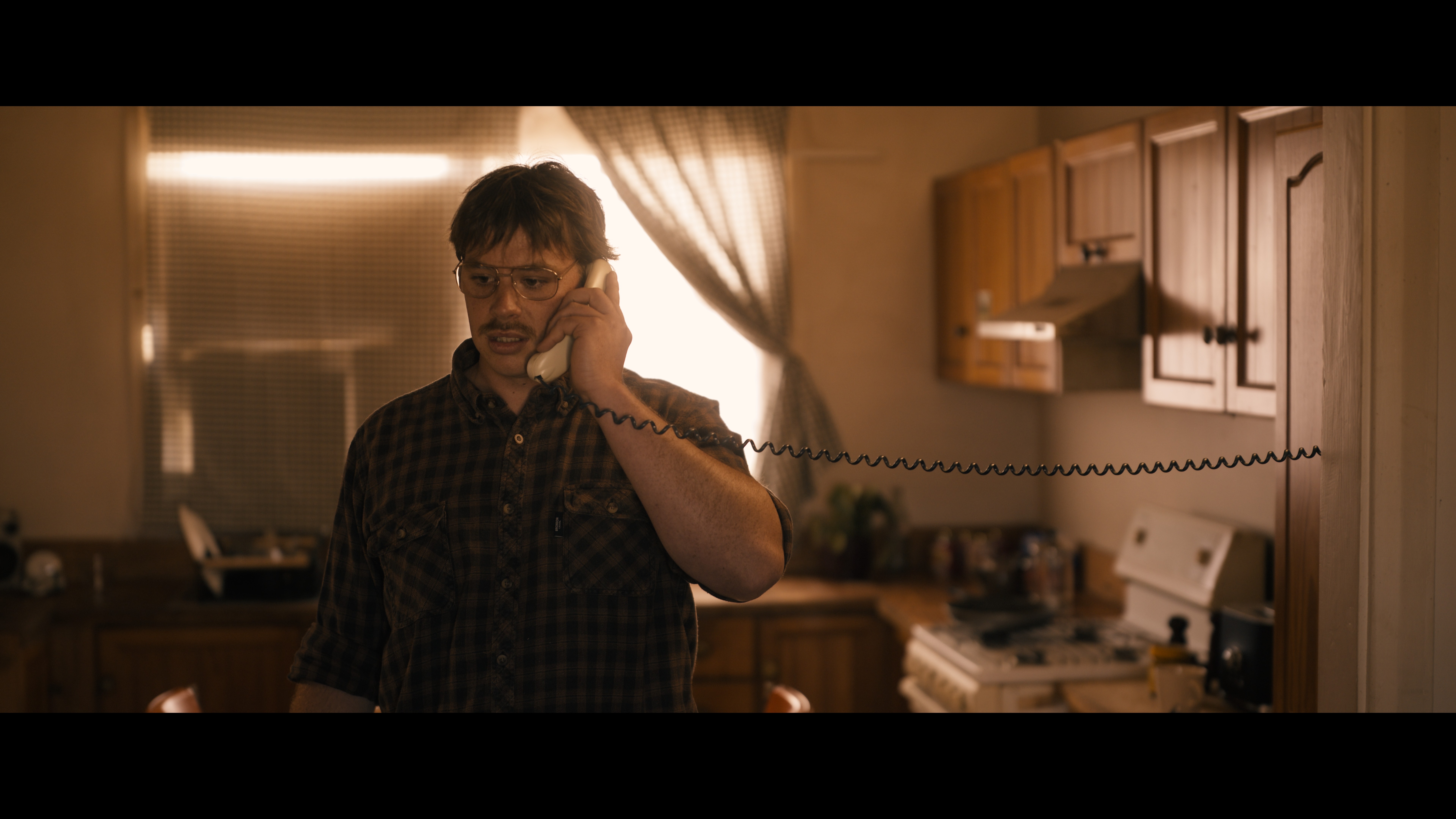 A person stands against a vibrant background of orange and yellow wavy patterns. They are wearing a dark coat, looking contemplative and thoughtful.