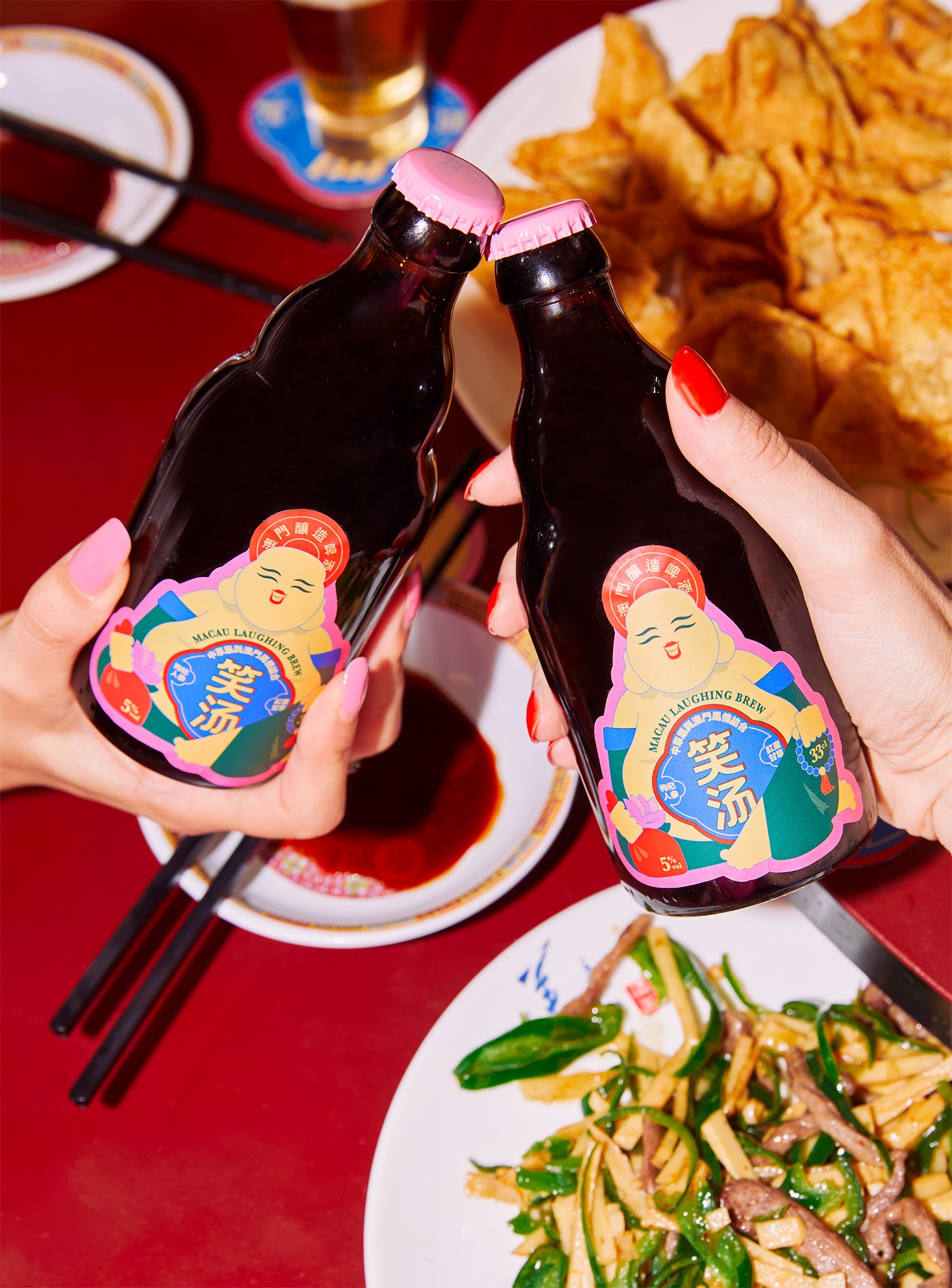 Two people clinking Macau Laughing Brew bottles over a red background.