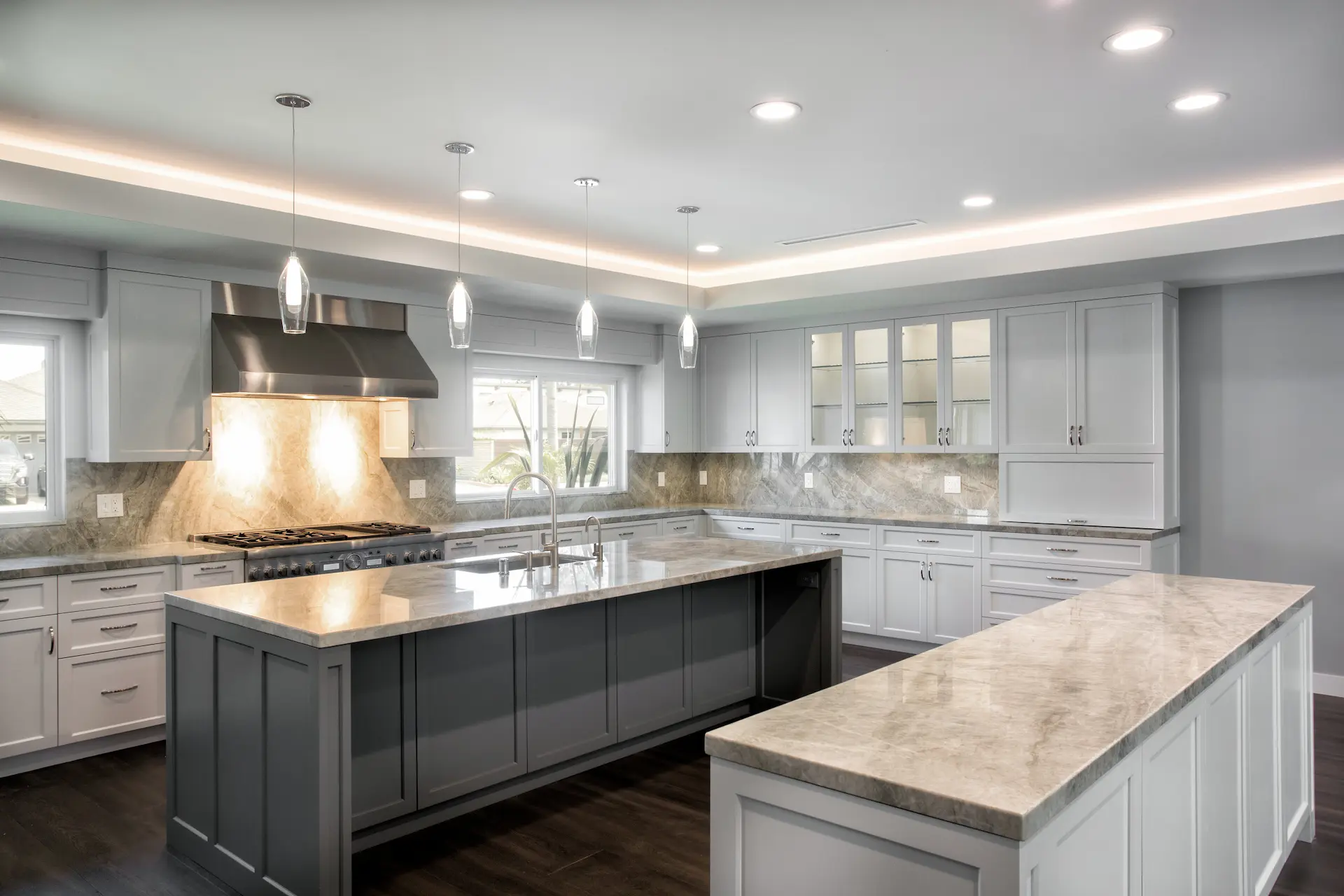 Spacious kitchen with white cabinetry, central island, hardwood floors, and pendant lighting in Costa Mesa Remodel. Photo by Chris Darnall.