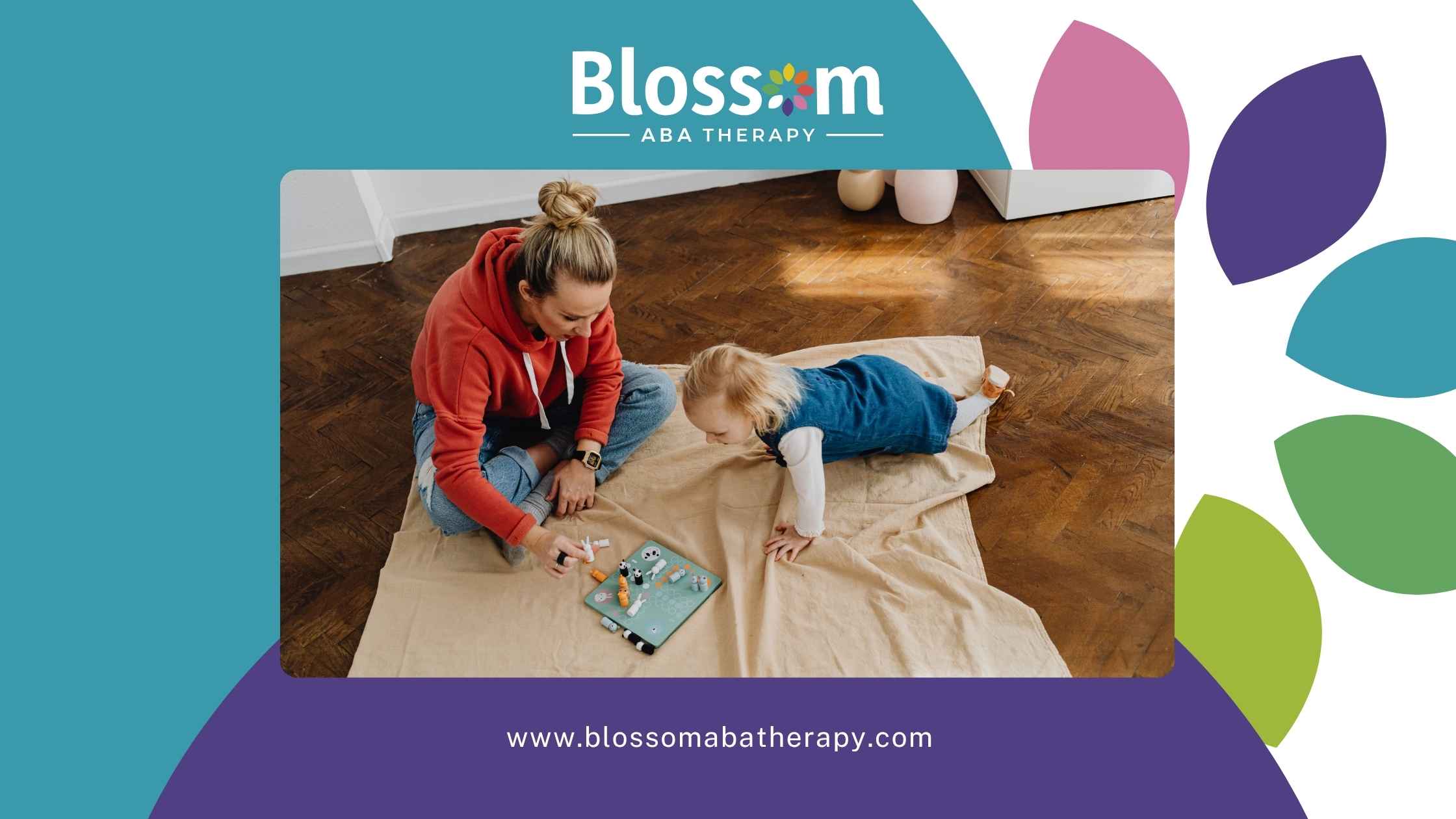 A woman in a red hoodie plays with a young child on a blanket-covered floor.