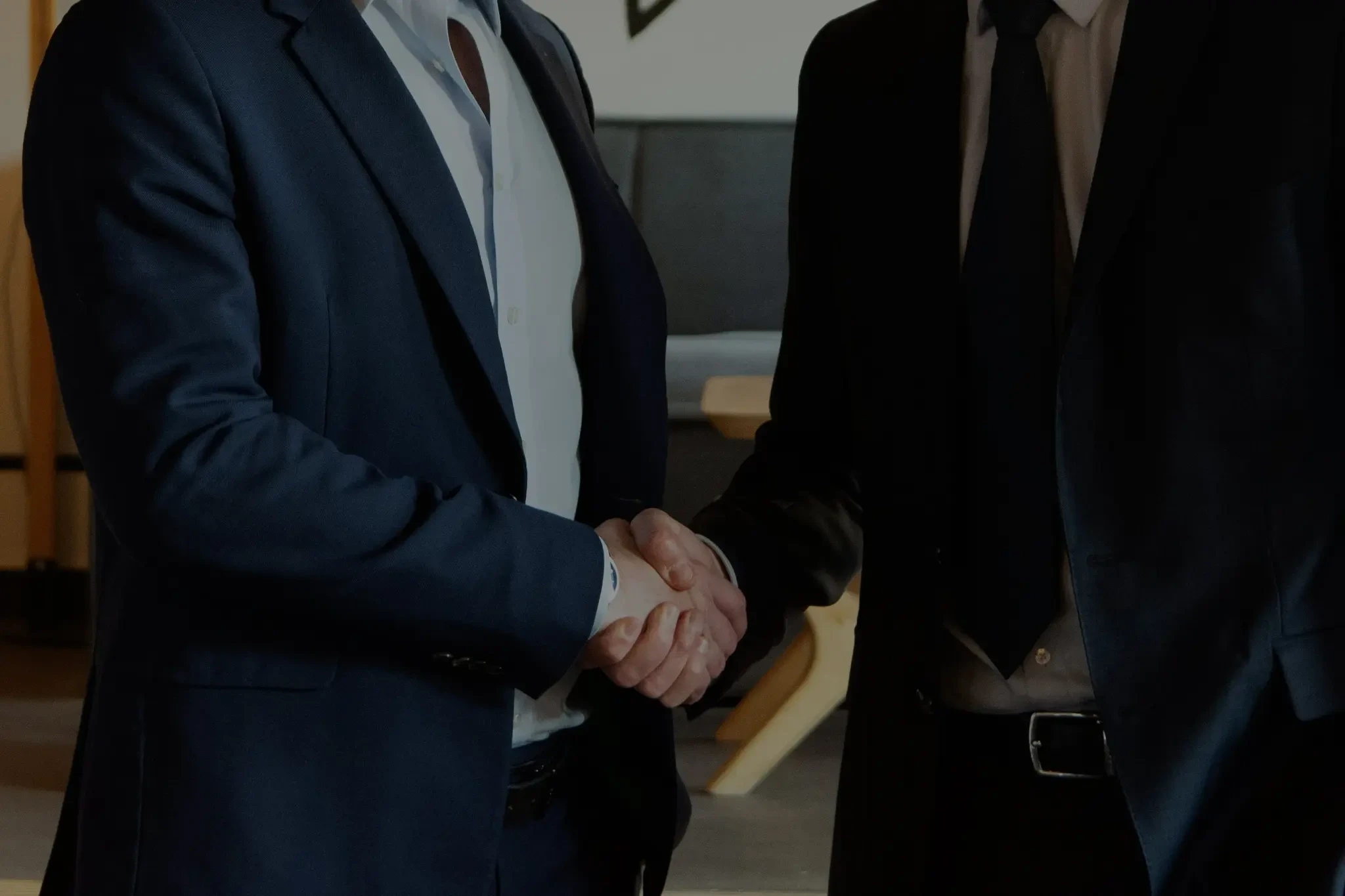 Two formally dressed people shake hands in an office.