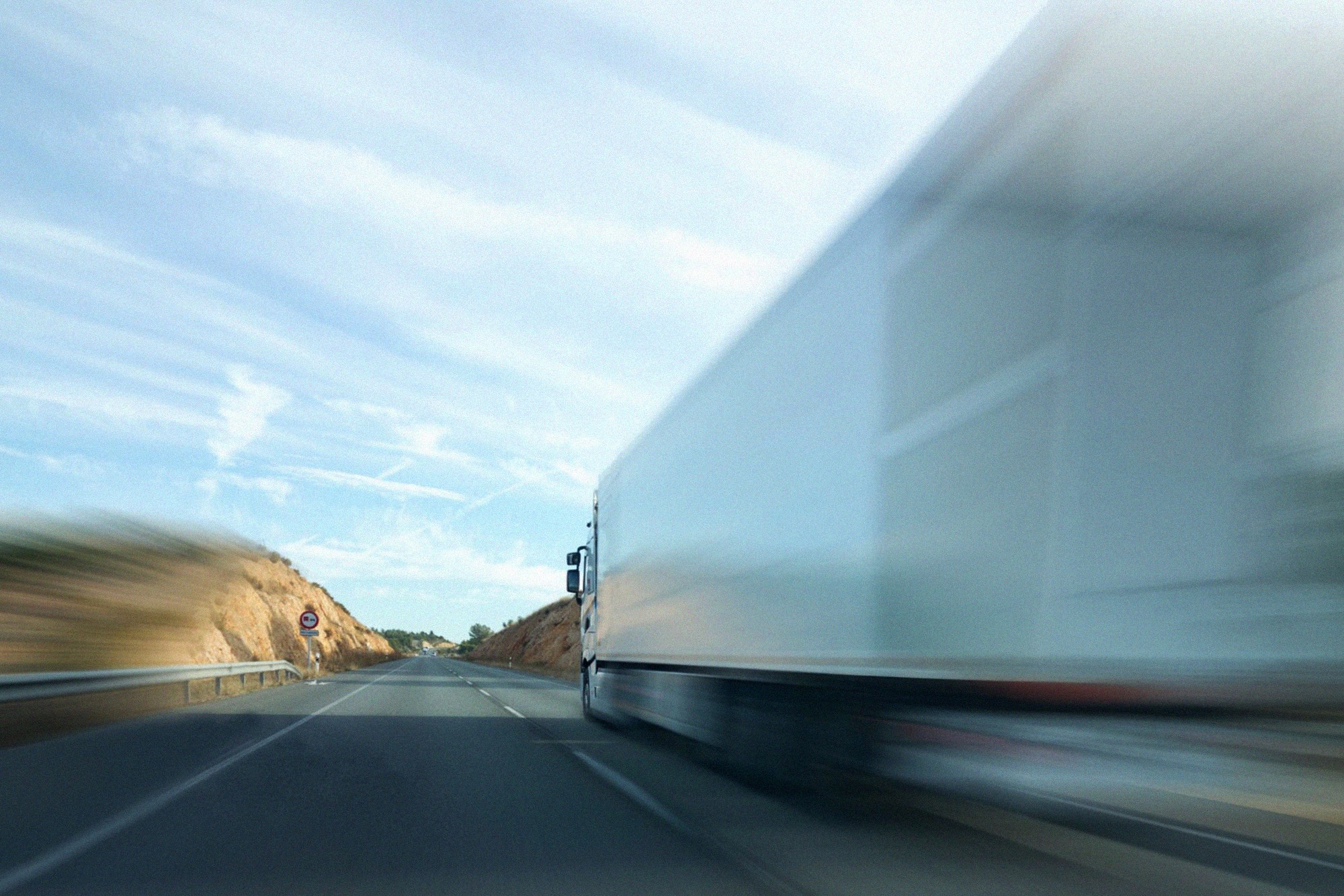 Truck speeding along an open road with motion blur under a wide blue sky, symbolising efficient transport services.