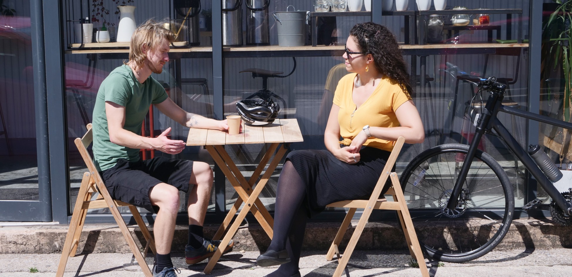 Two people sitting at outdoor tables, one holding a small object.