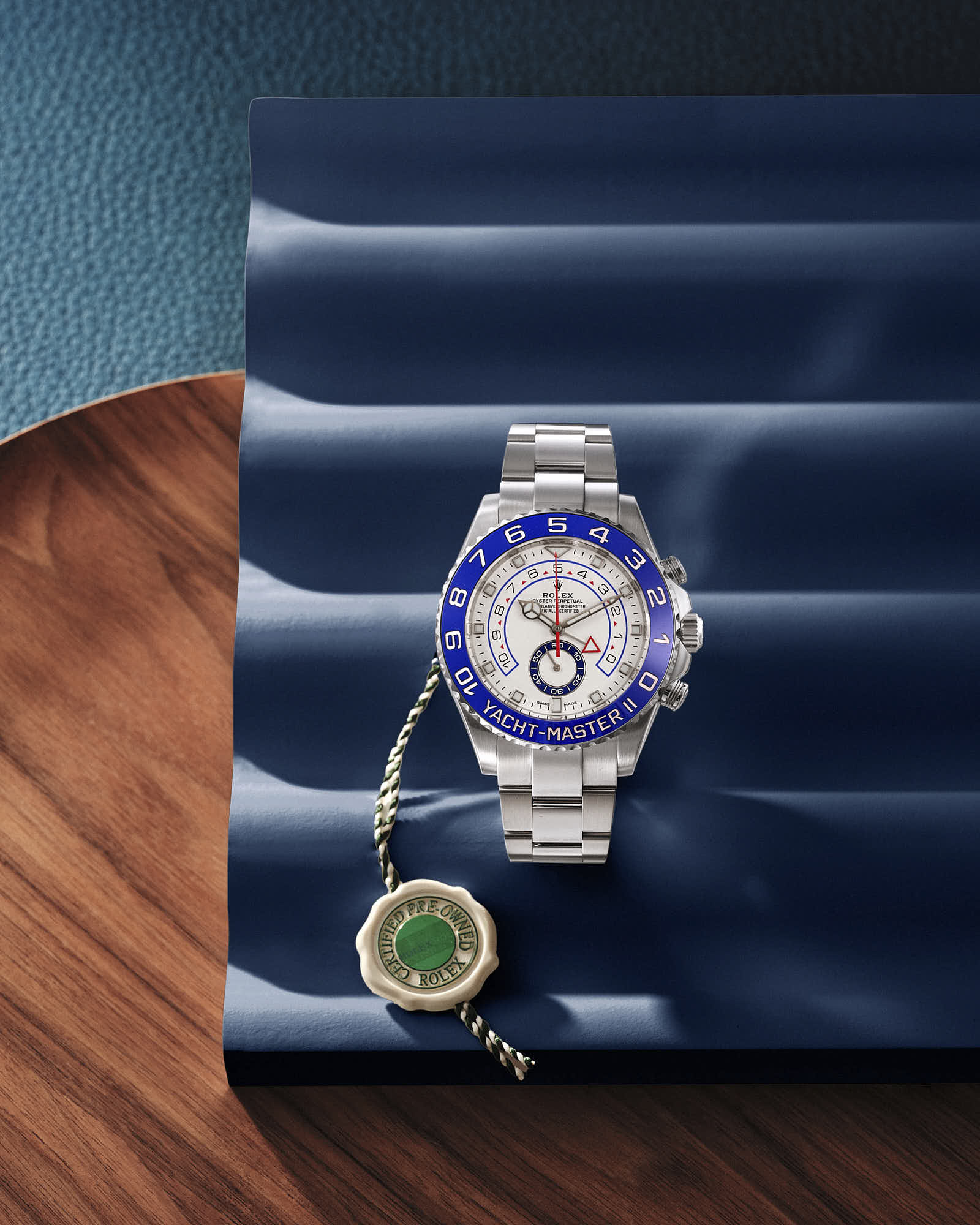 Luxury silver Rolex Yacht-Master II watch with blue bezel on textured background.