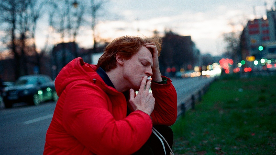 Analog street photography of a young person smoking on a Berlin avenue with cinematic mood