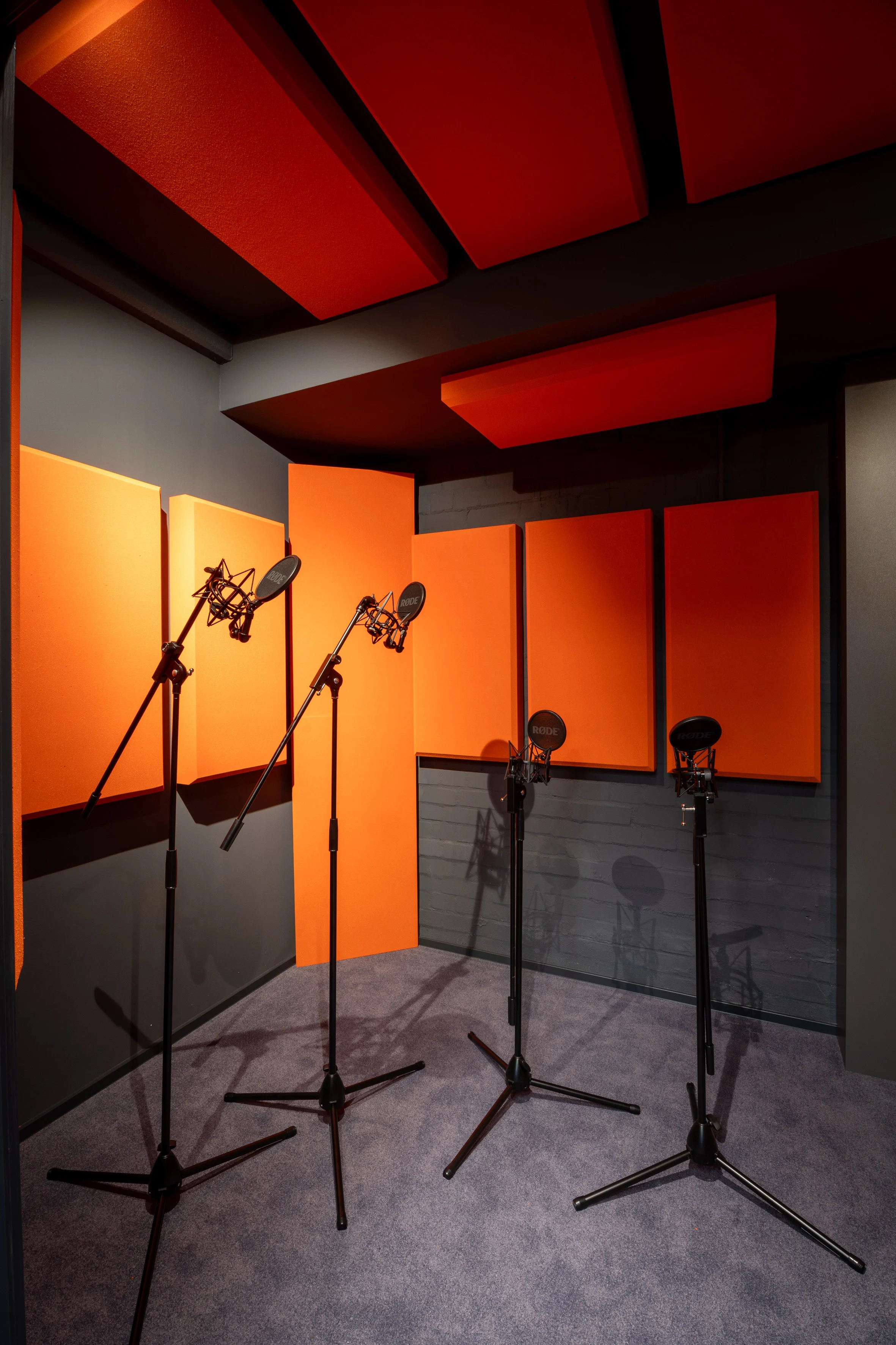 Recording room at SNIPES BASEMENT with microphone stands and pop filters, surrounded by orange acoustic panels on grey walls and ceiling.
