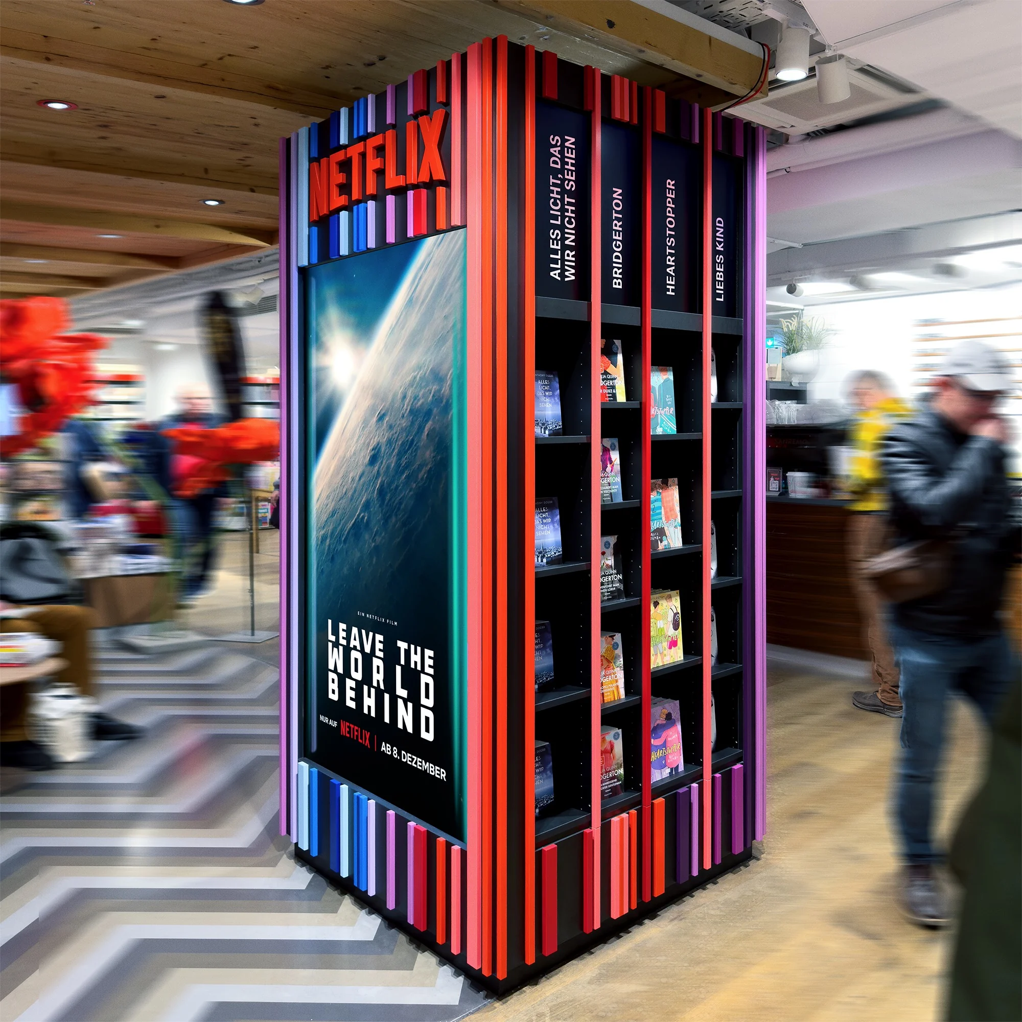 Netflix in-store book display in a bookshop, vertical multi-coloured stripe column featuring the „Leave The World Behind" poster and shelves of related novels.