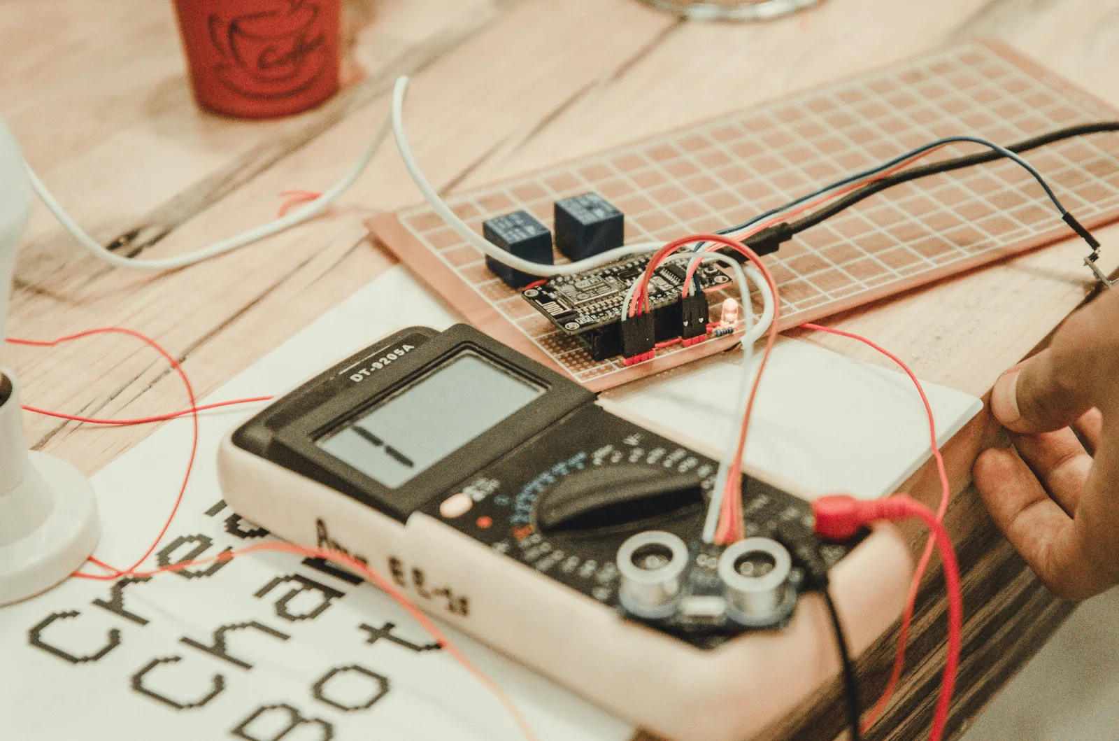 Person testing circuit board with multimeter and probes on desk
