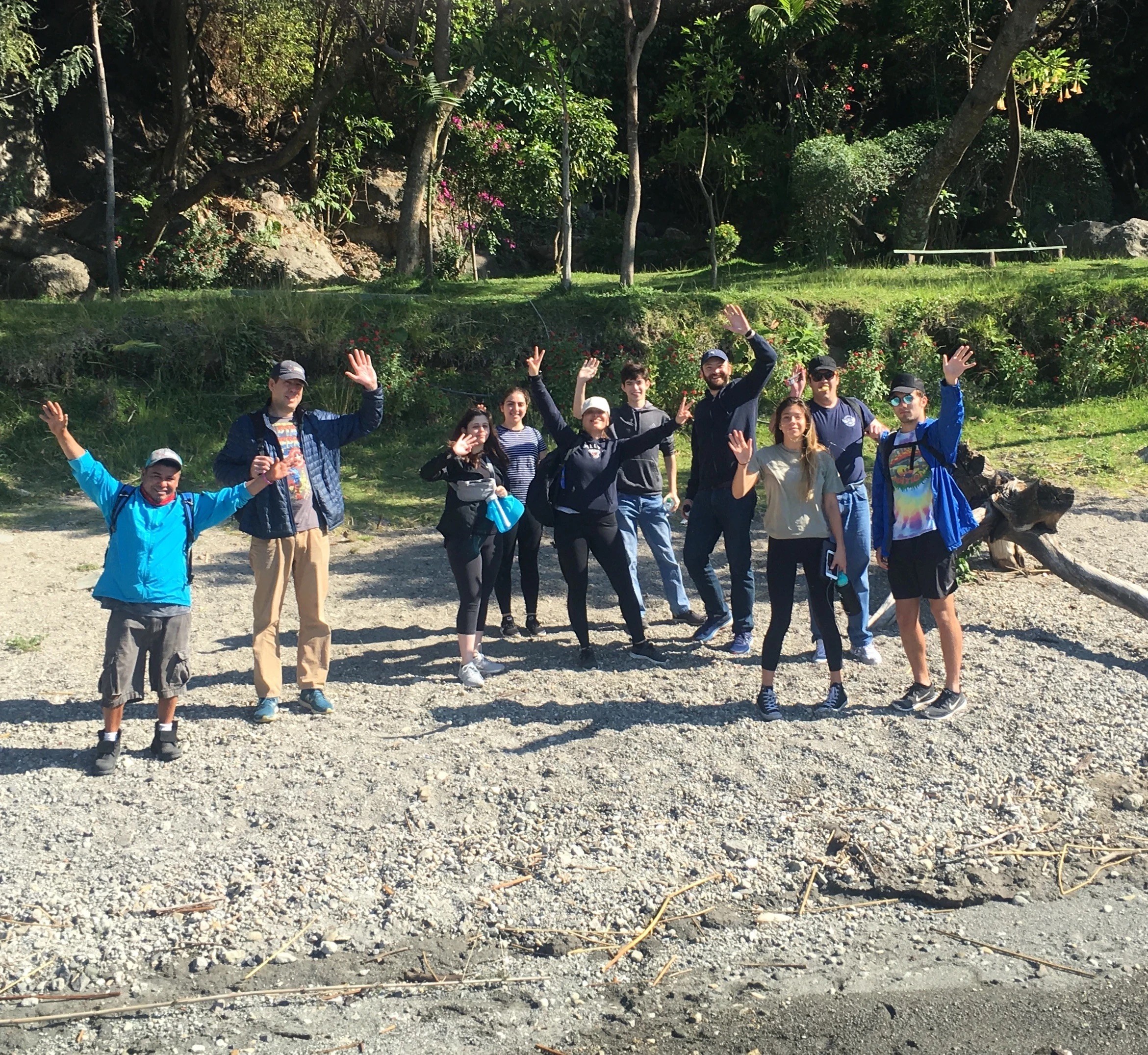 A group of people together on a beach, smiling and waving at the camera under a sunny sky.