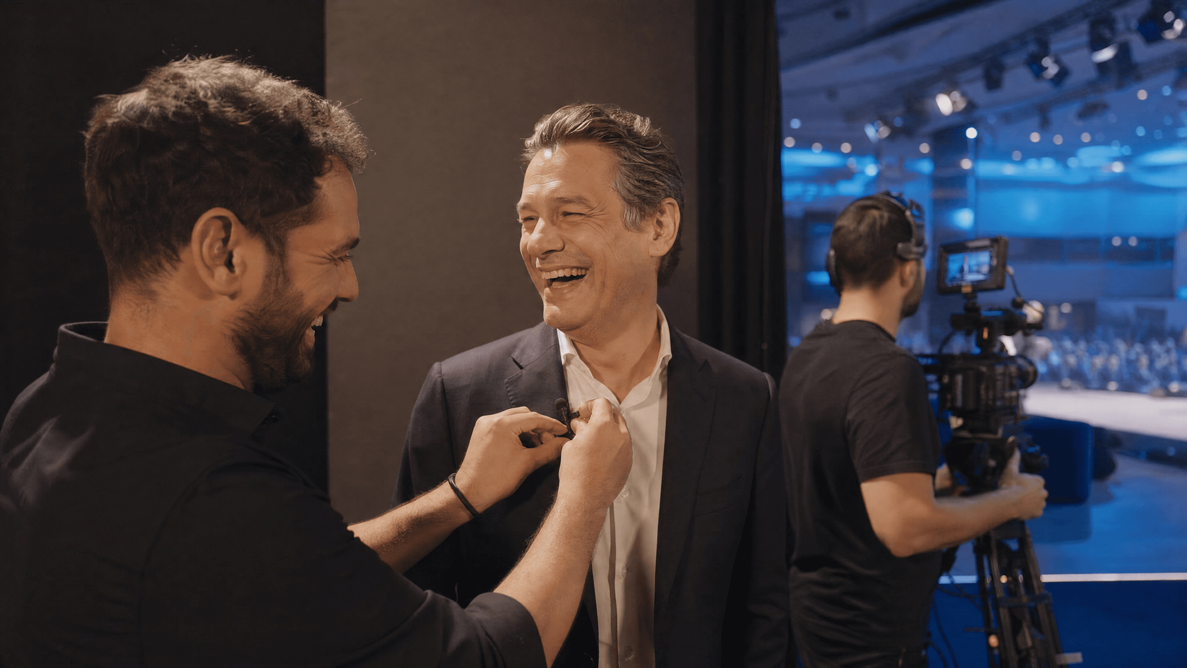 Sound engineer attaching a lavalier microphone to a smiling corporate speaker before filming