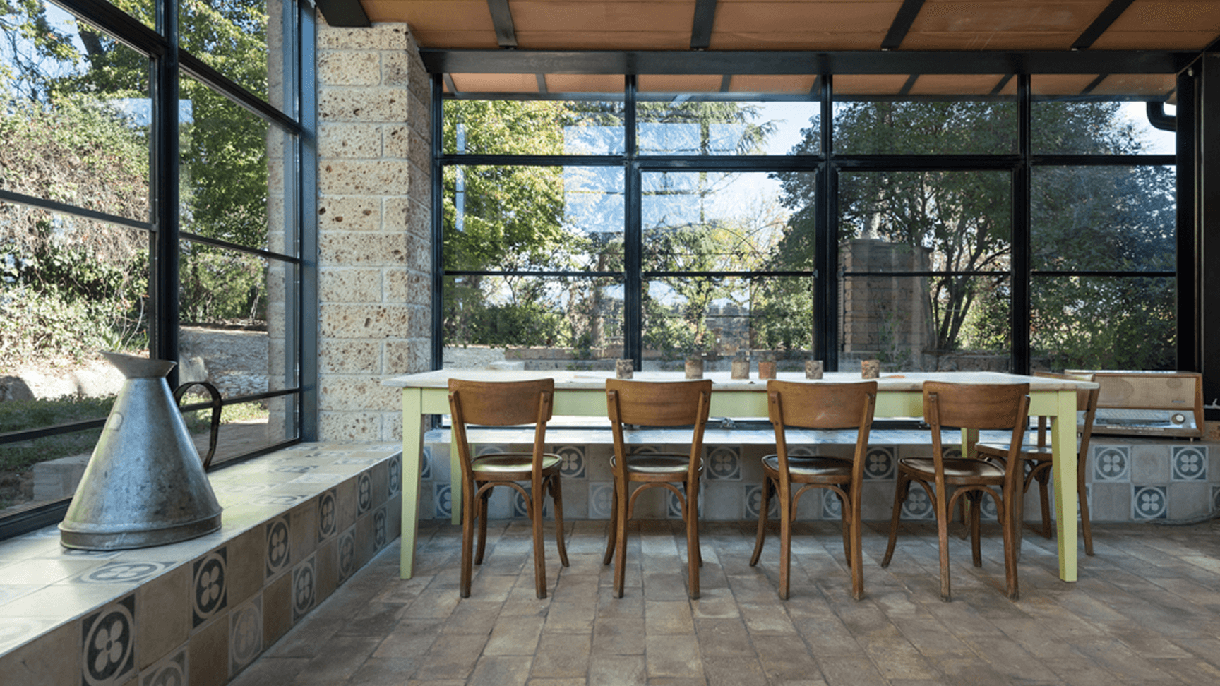 A modern interior featuring a long wooden bar with stools next to large windows, providing natural light.