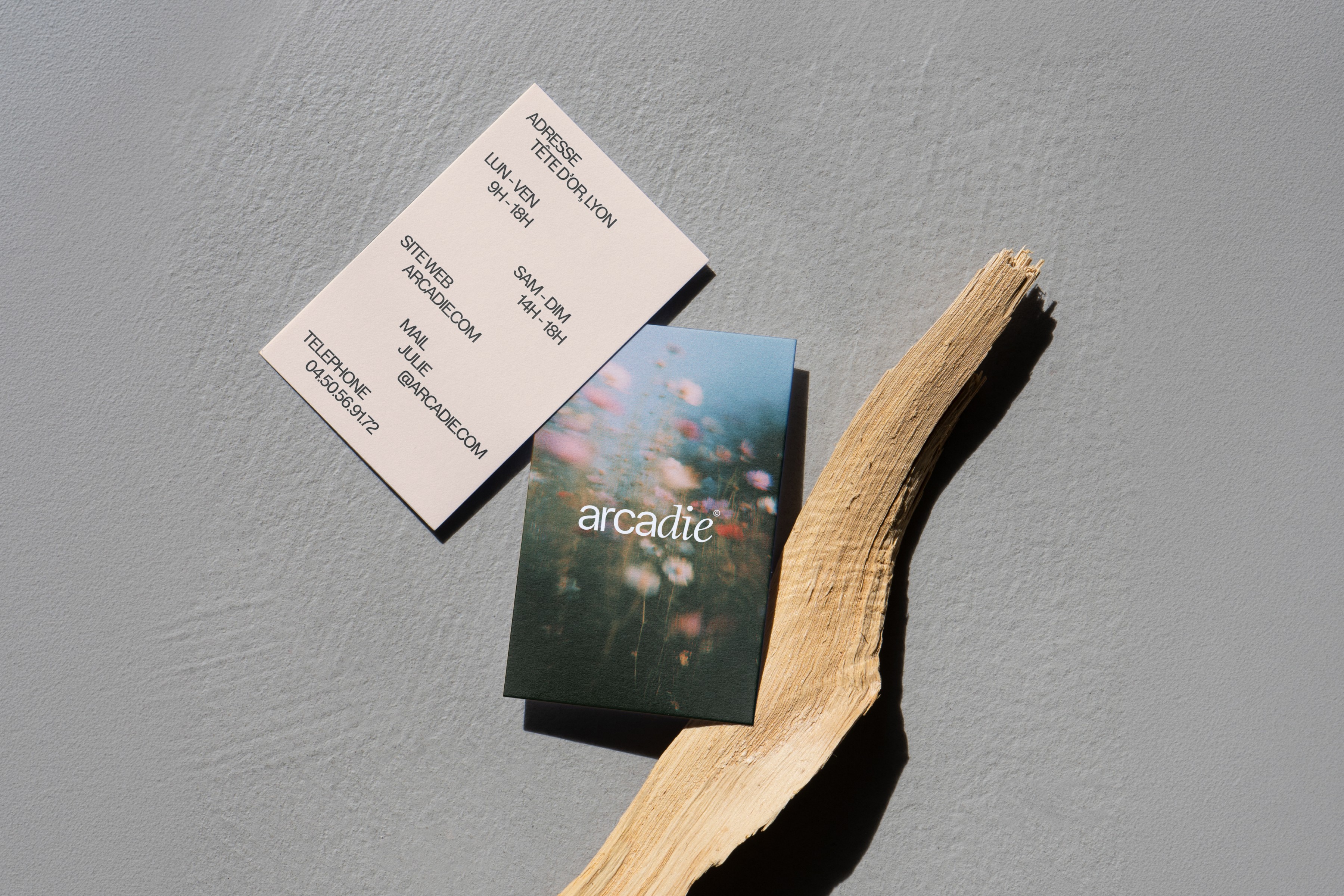 Cartes de visite minimalistes arcadie posées près d’un bois flotté, papeterie élégante pour studio de yoga et bien-être.