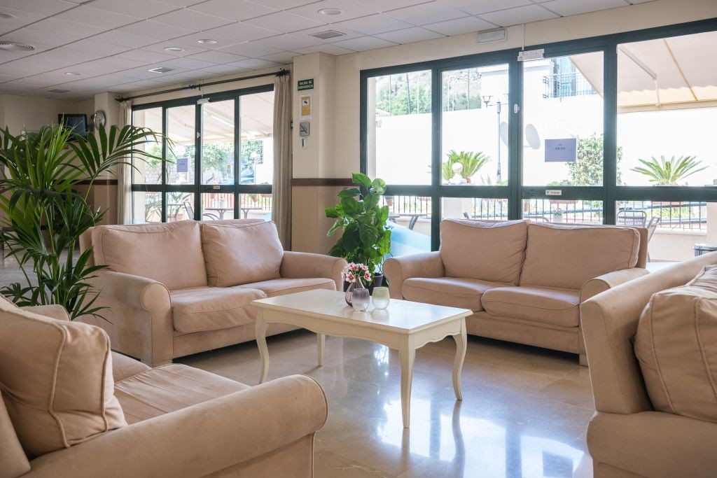 Comfortable lounge with beige sofas, a white coffee table, and large windows with garden views.