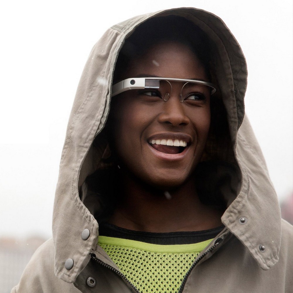 A hooded woman is smiling and wearing Google Glasses.