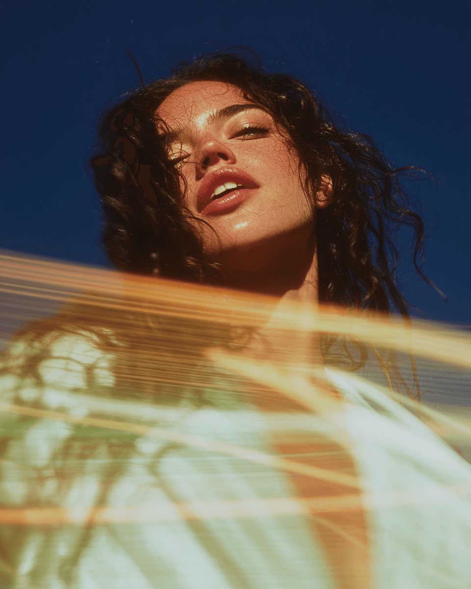 Close-up portrait of a woman with curly hair and golden light flares across the frame.
