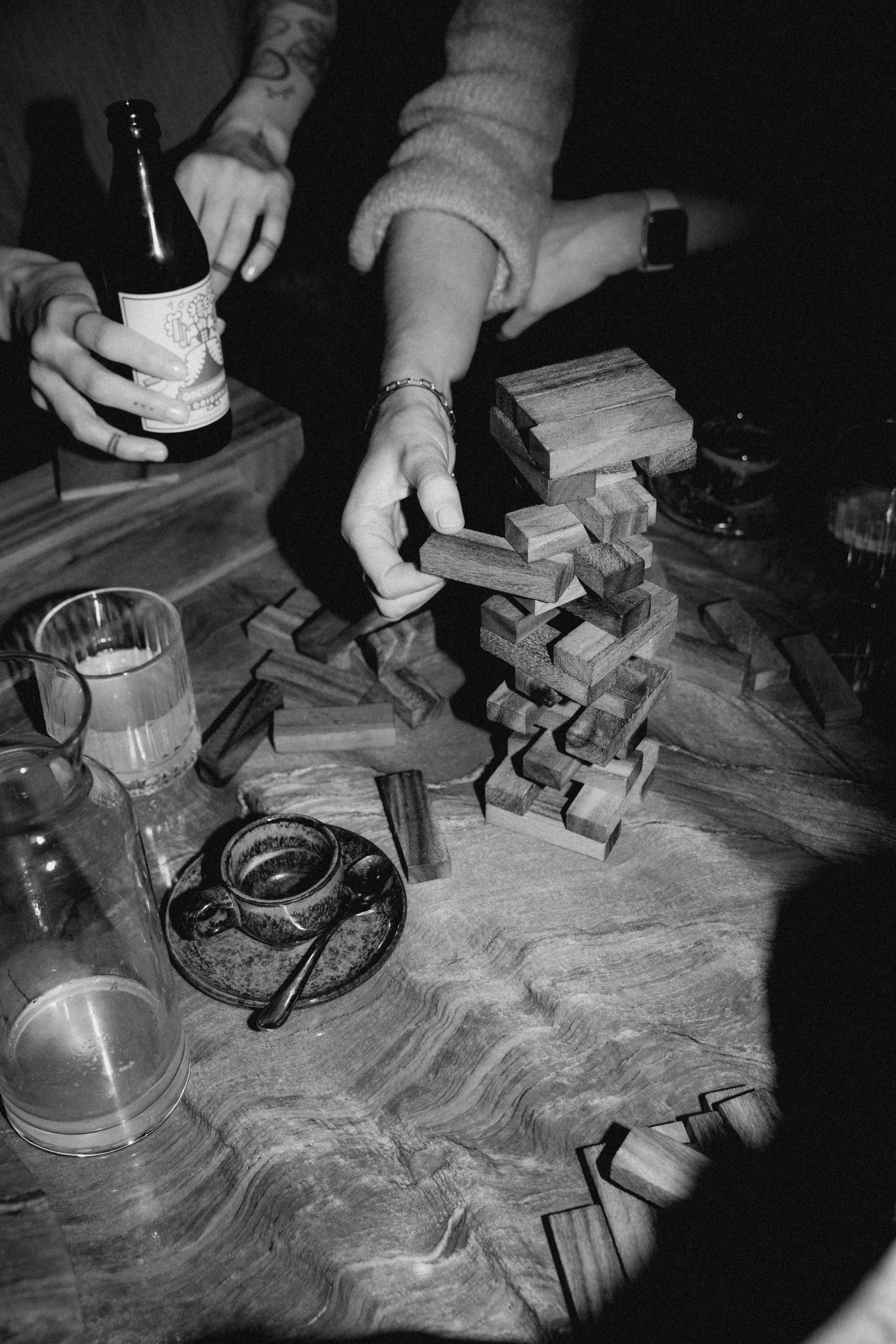 Black and white photograph of friends playing a wood stacking game and enjoying drinks, with the caption 'FRIENDS'