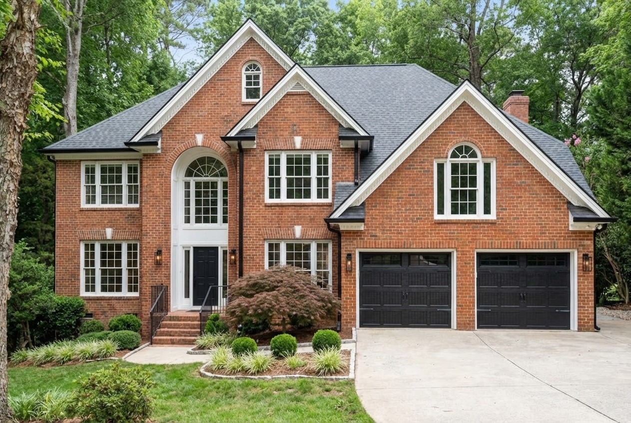 1990s brick house modernized — black carriage garage doors, charcoal shutters, matte black accents