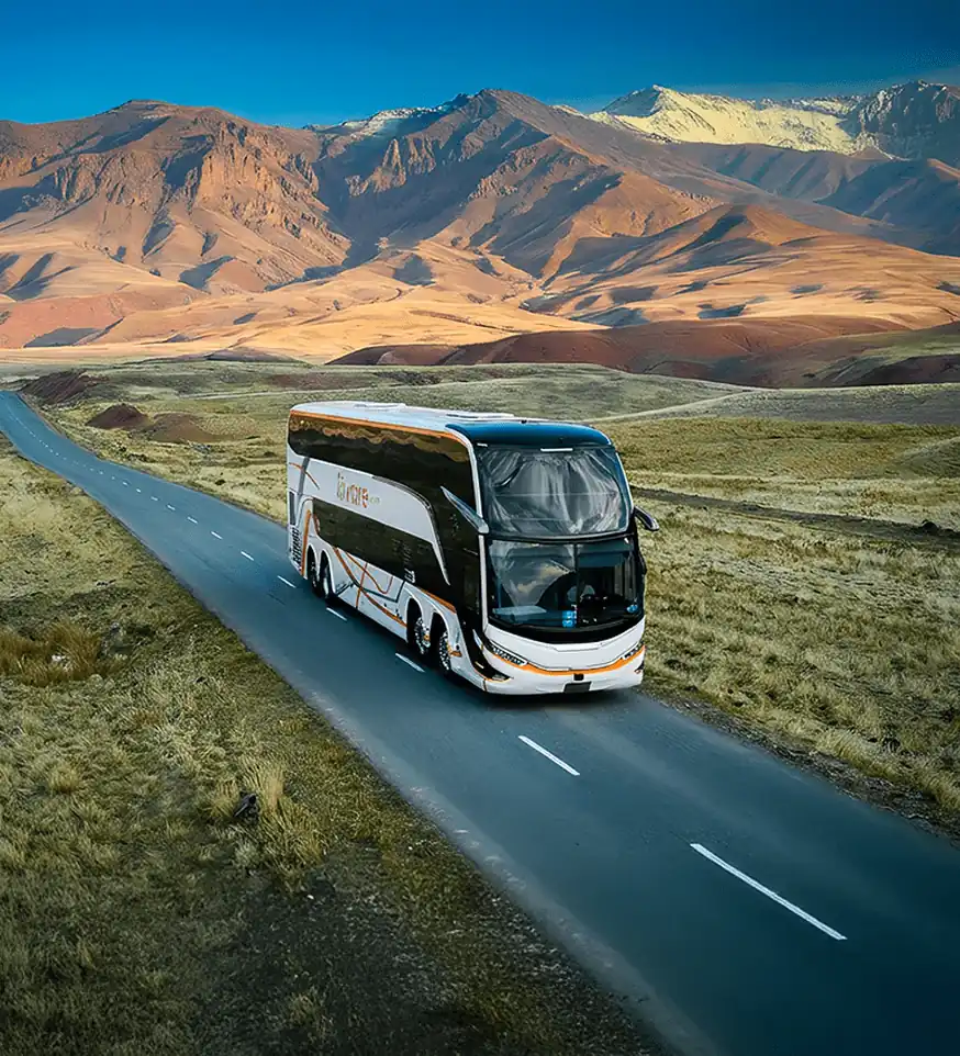 Ônibus de turismo rodoviário em estrada aberta cruzando paisagem montanhosa da Cordilheira dos Andes