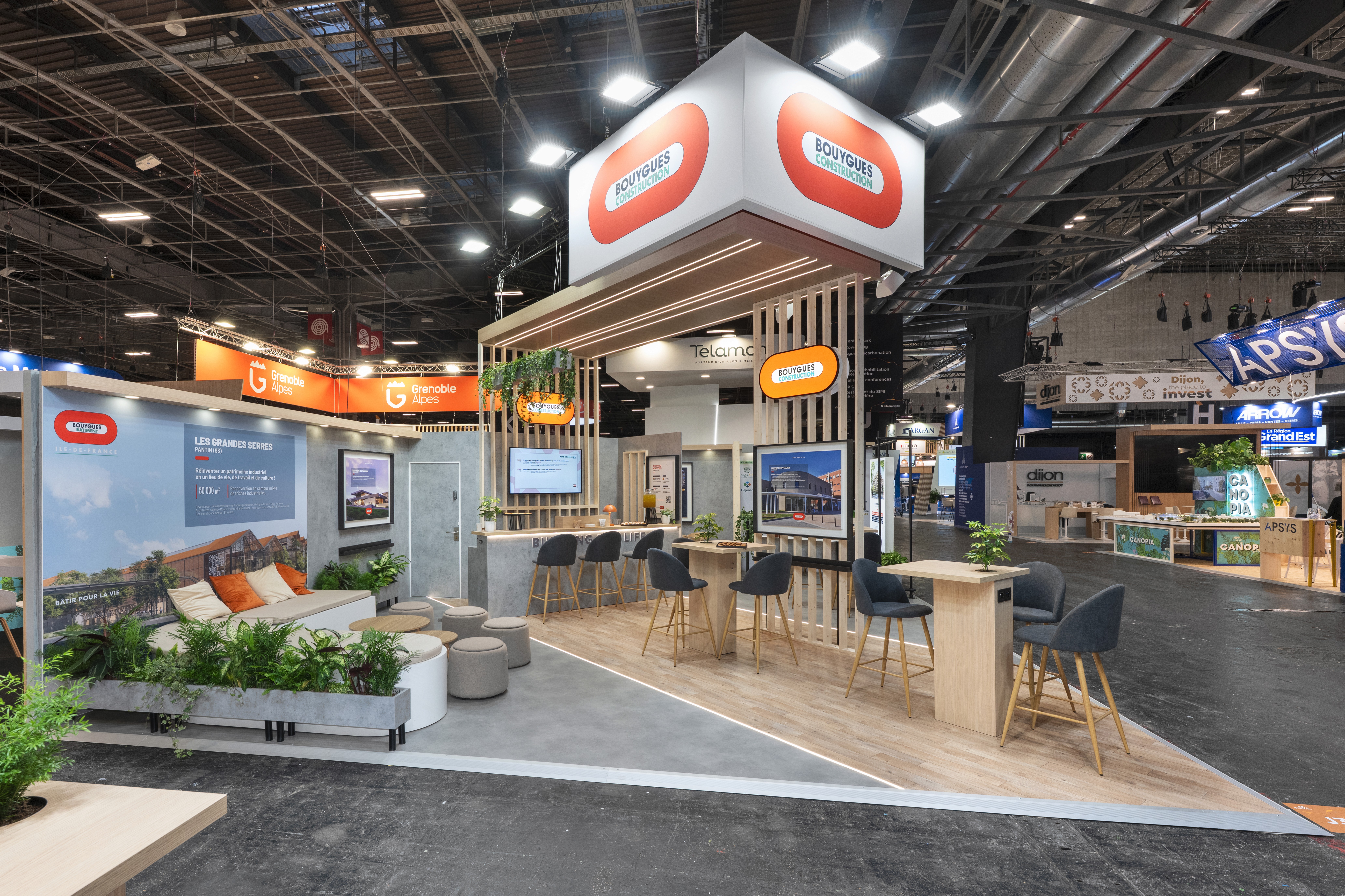 Stand Groupe Bouygues SIMI 2025 Paris par Expace – vue d'ensemble avec zone lounge fauteuils ronds, écrans grands formats projets immobiliers et identité orange vif