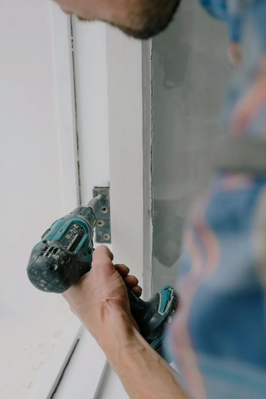 Worker drilling hinge screws into door frame with cordless drill