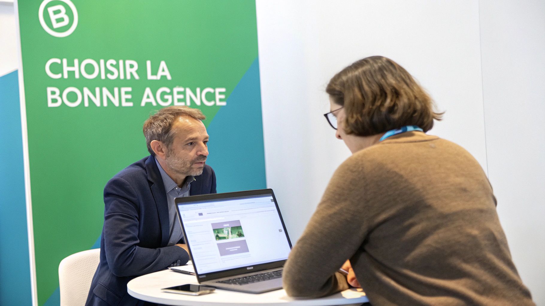 Deux professionnels discutent devant un écran d'ordinateur, avec une bannière 