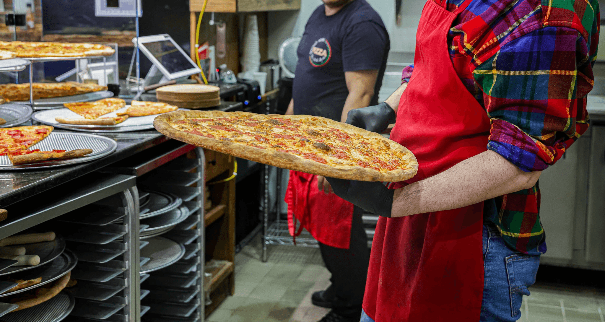 A pizzaiolo sliding a large pizza into a glowing hot brick oven using a wooden peel