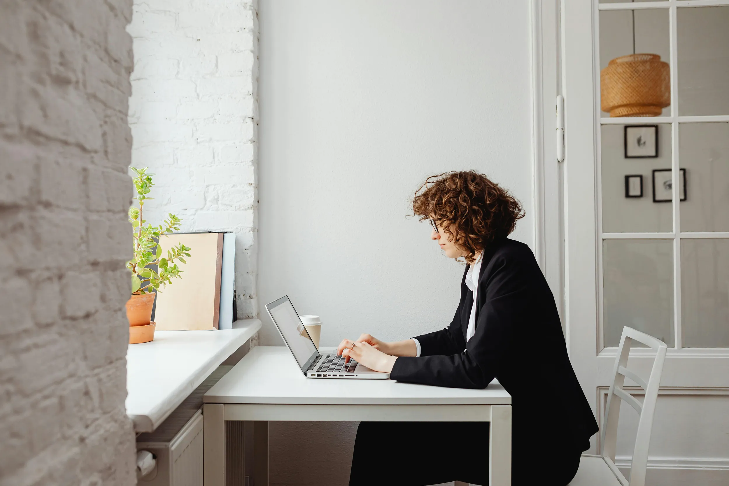 Woman typing on laptop in bright minimalist home office, calm remote working atmosphere