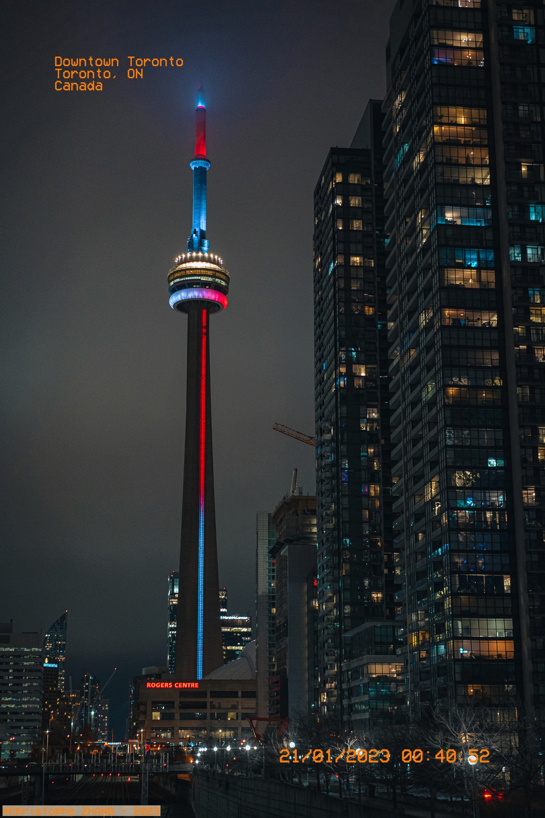 Vue nocturne de la tour CN illuminée, entourée de gratte-ciel à Toronto.