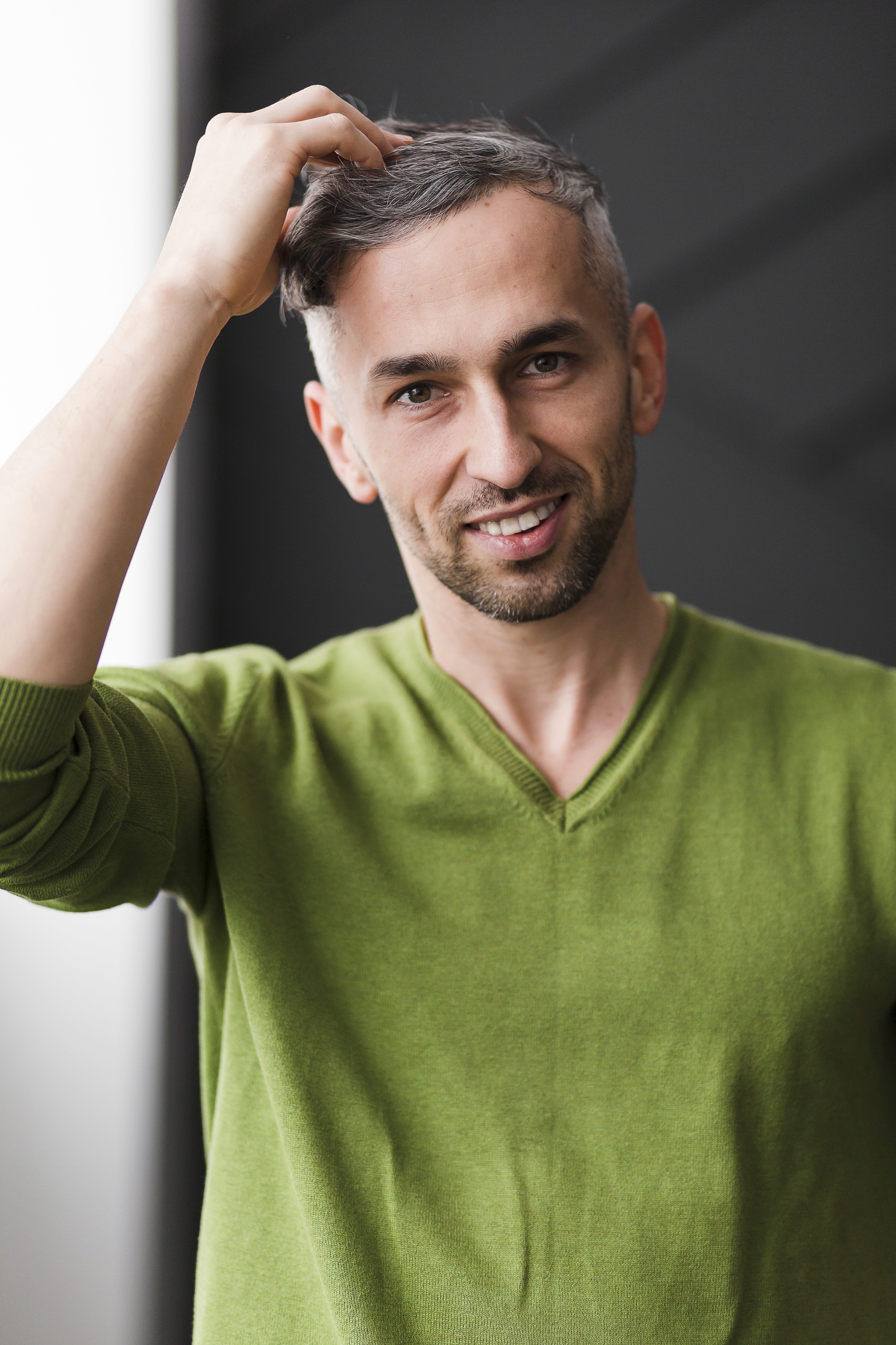 A smiling young man with crossed arms, wearing a plaid shirt and white t-shirt, poses against a dark background.