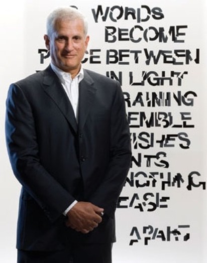 A photo of a man in a suit standing in front of some wall with text on it.