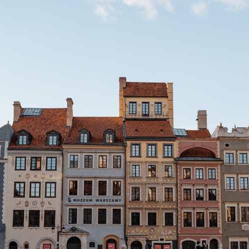 A row of historic European buildings with colorful facades and red-tiled roofs against a clear sky.