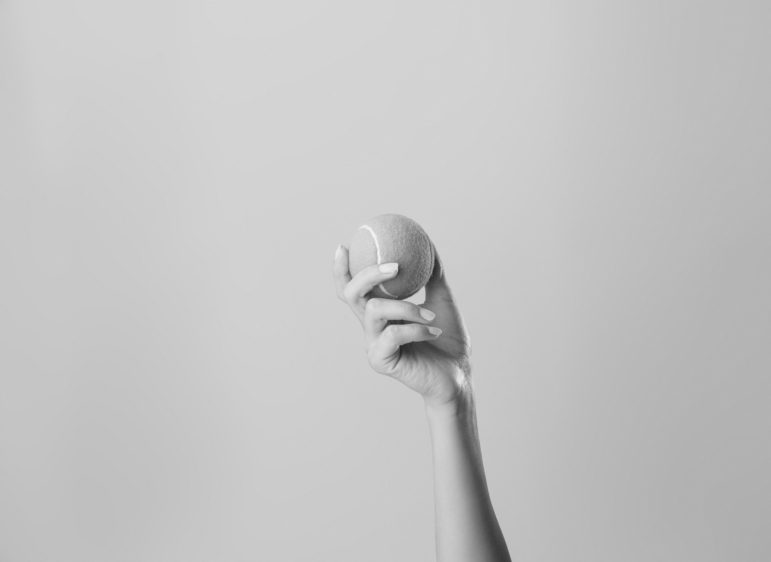 A black and white photo of a hand holding a tennis ball against a plain background.