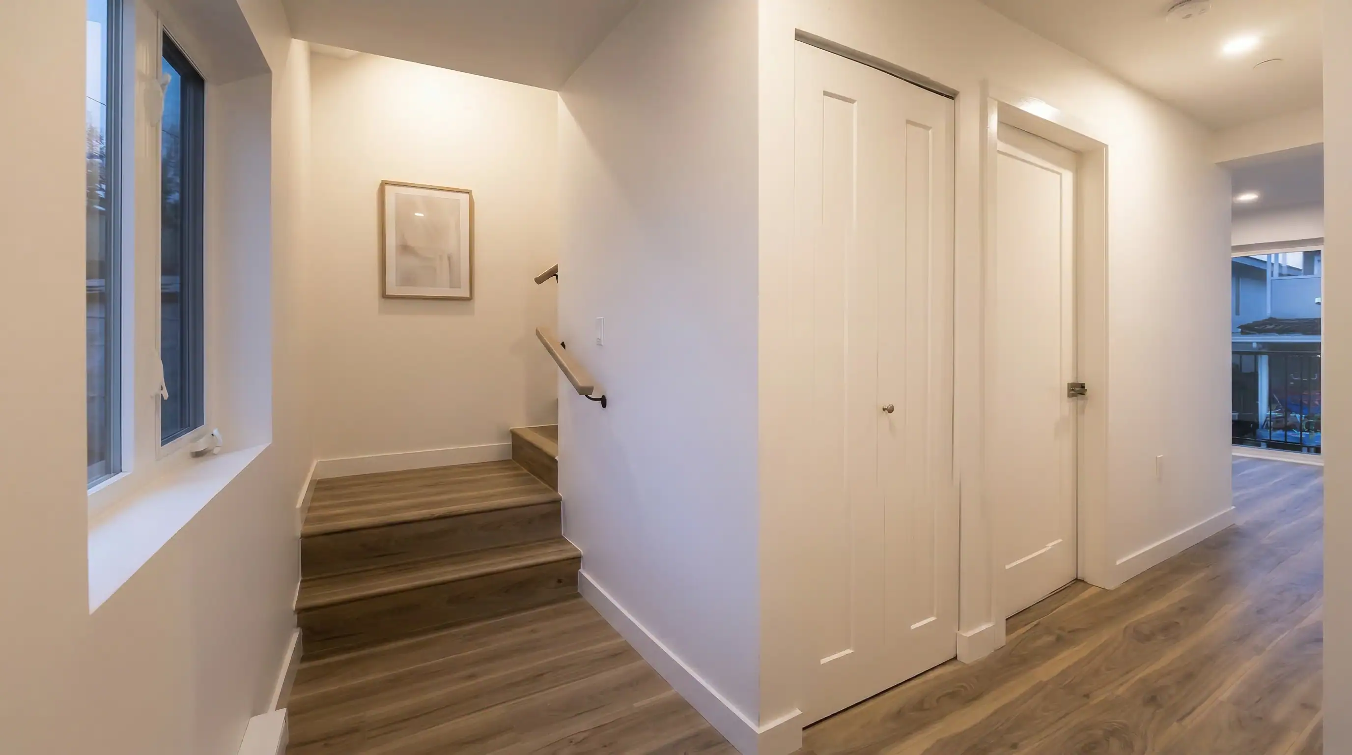 Interior staircase and hallway of the East 63rd laneway home by Vancouver Custom Homes, showing wood-tread stairs, white walls, and a bright corridor leading toward the rear patio.